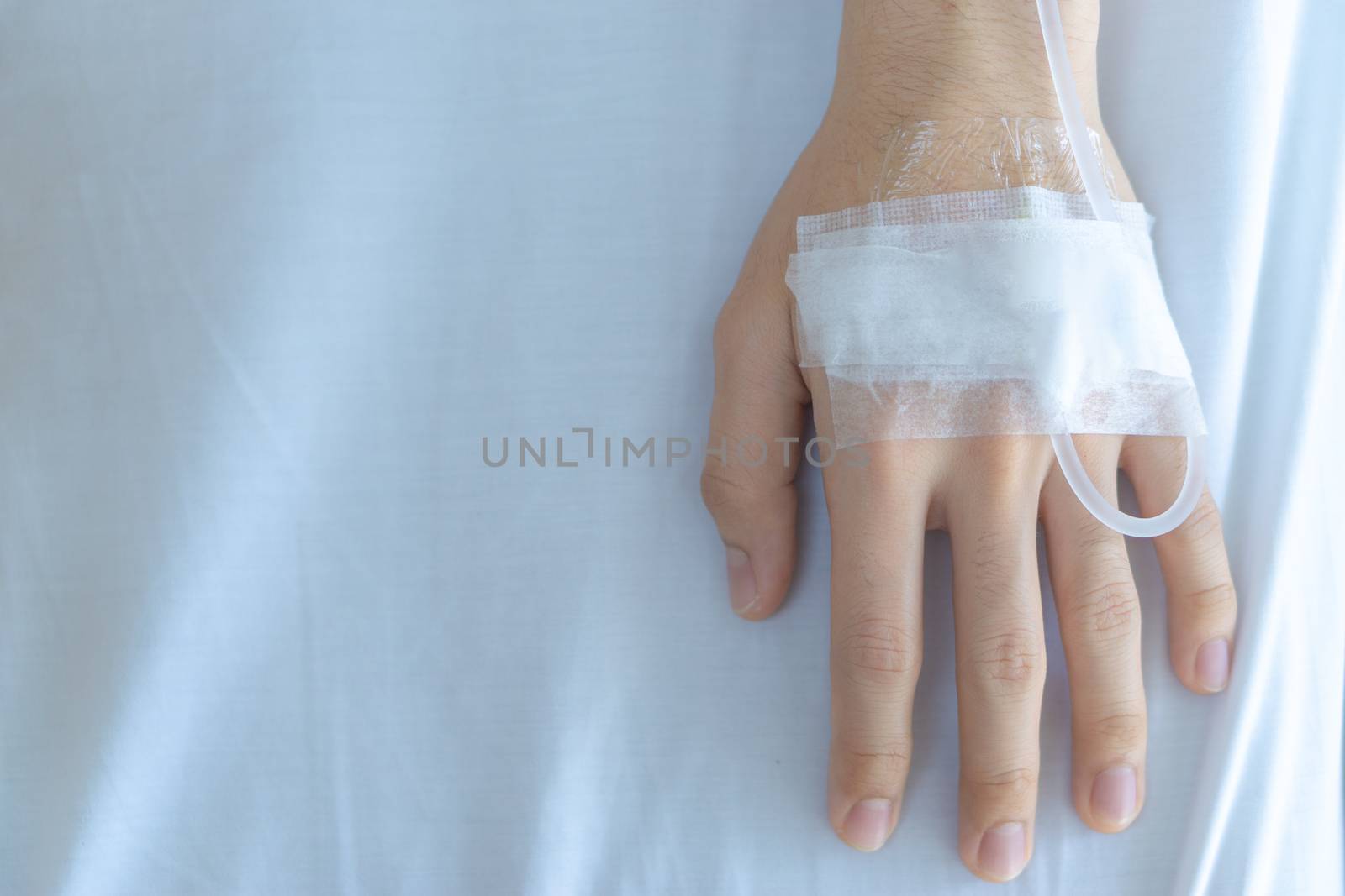 Patient hand with the tube of normal saline infusion on with cloth background at the hospital. Sick and health concept