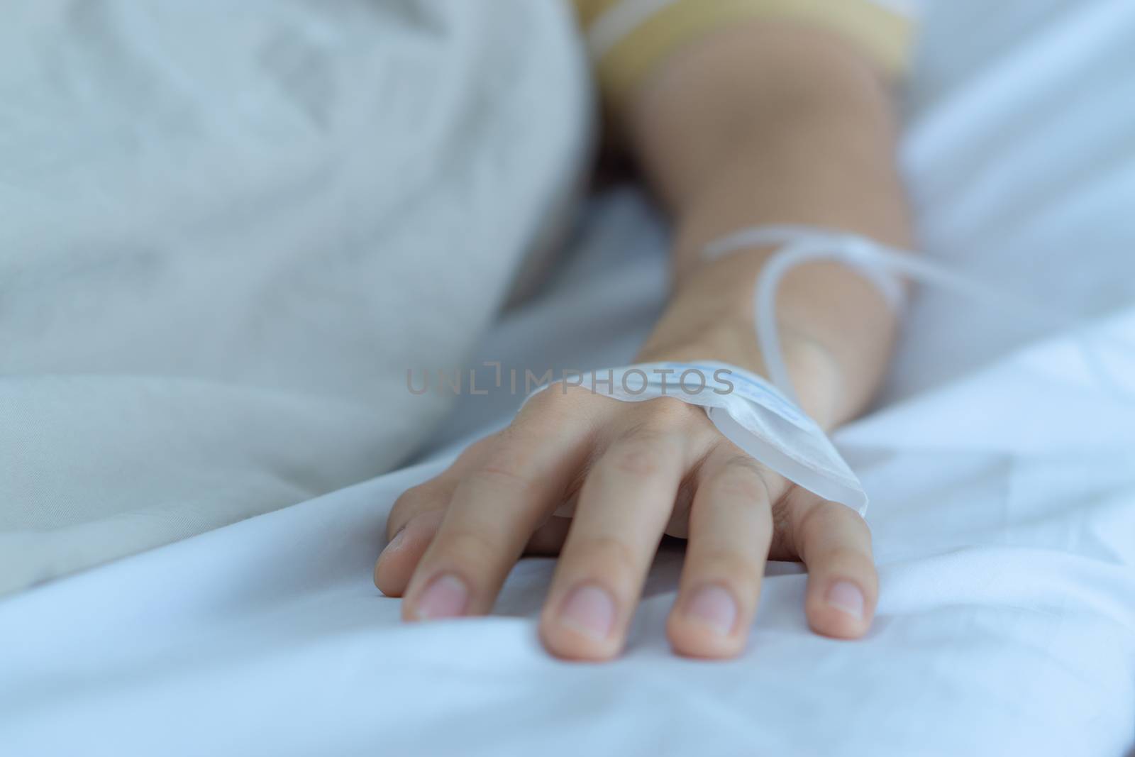 Patient hand with the tube of normal saline infusion on with cloth background at the hospital. Sick and health concept