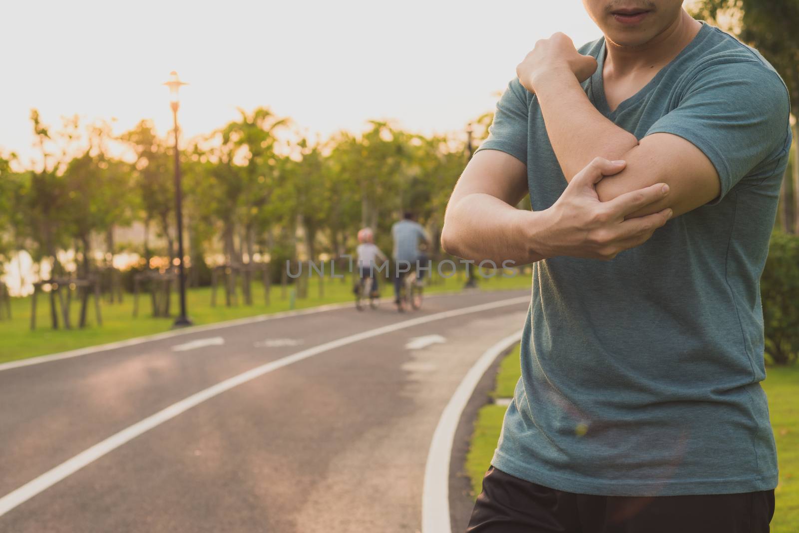 A male athlete suffering from arm and elbow pain and injury at the park. Sport and healthcare concept.