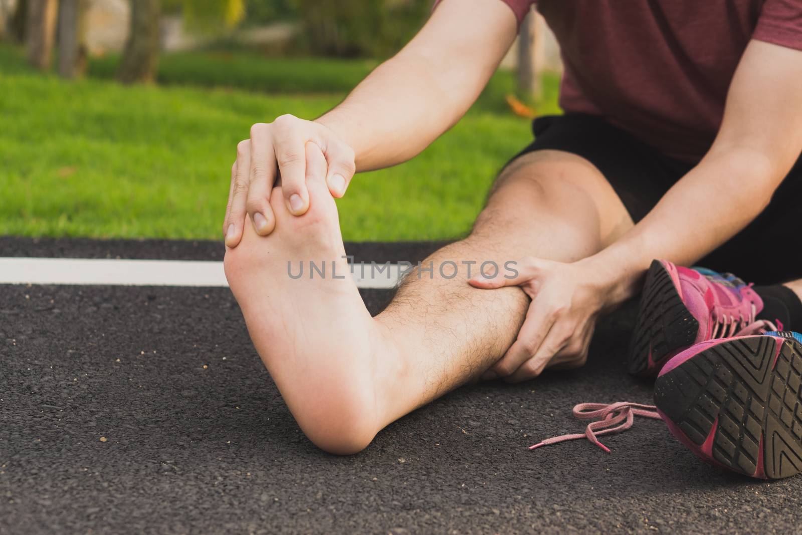 Young man massaging his painful foot from jogging and running on running track. Sport and exercise concept.