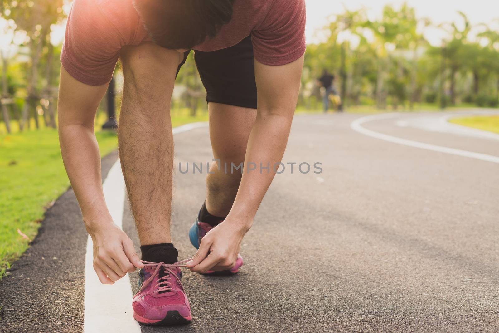 The male athlete is tying running shoes in the park with sunlight. Sport and exercise concept.