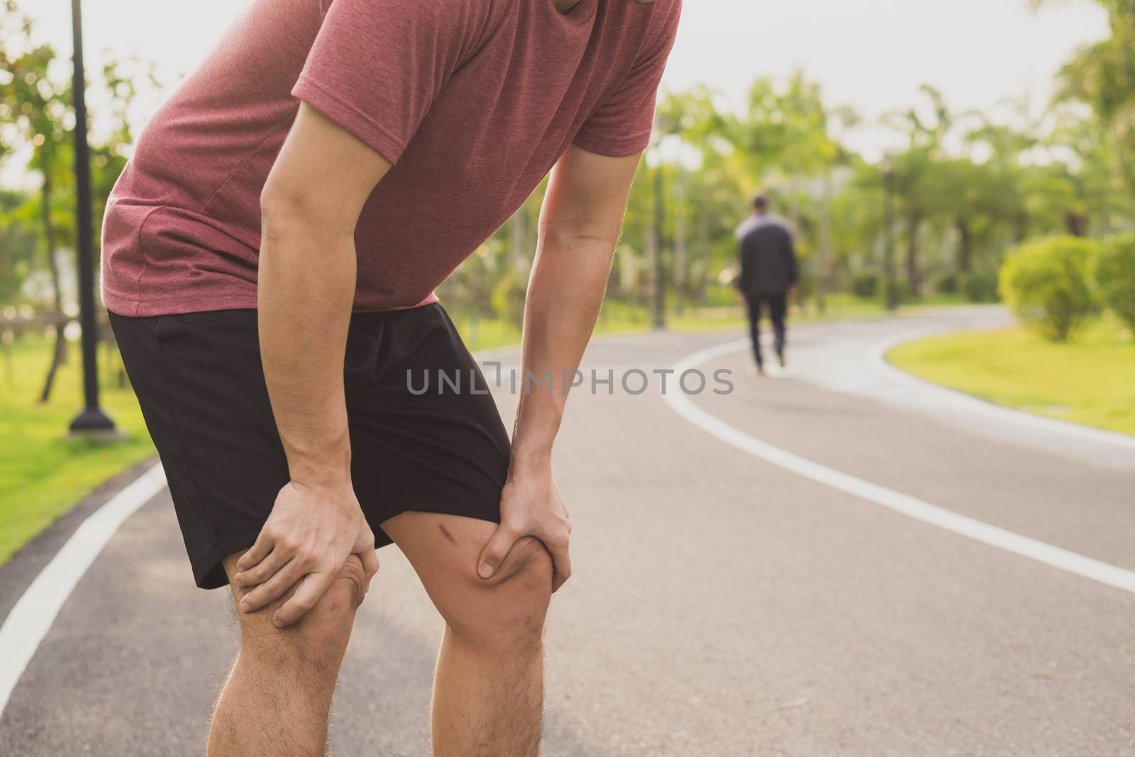 Knee Injuries. Young sport man holding knee with his hands in pain after suffering muscle injury during a running workout at park. Healthcare and sport concept.