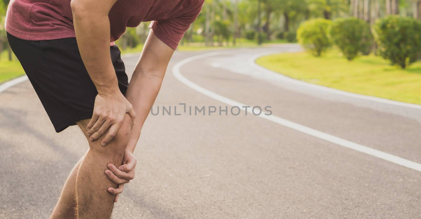 Knee Injuries. Young sport man holding knee with his hands in pain after suffering muscle injury during a running workout at park. Healthcare and sport concept.