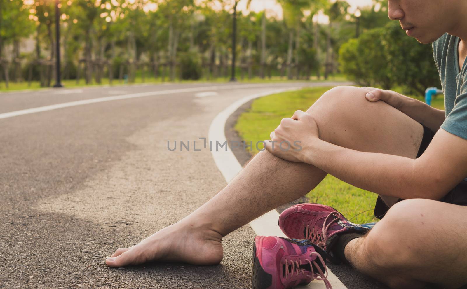 Knee Injuries. Young sport man holding knee with his hands in pain after suffering muscle injury during a running workout at park. Healthcare and sport concept.