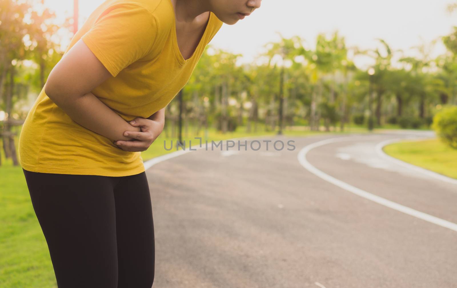 Sport womanman holding abdomen with her hands in stomach pain after running workout at park. Health care concept