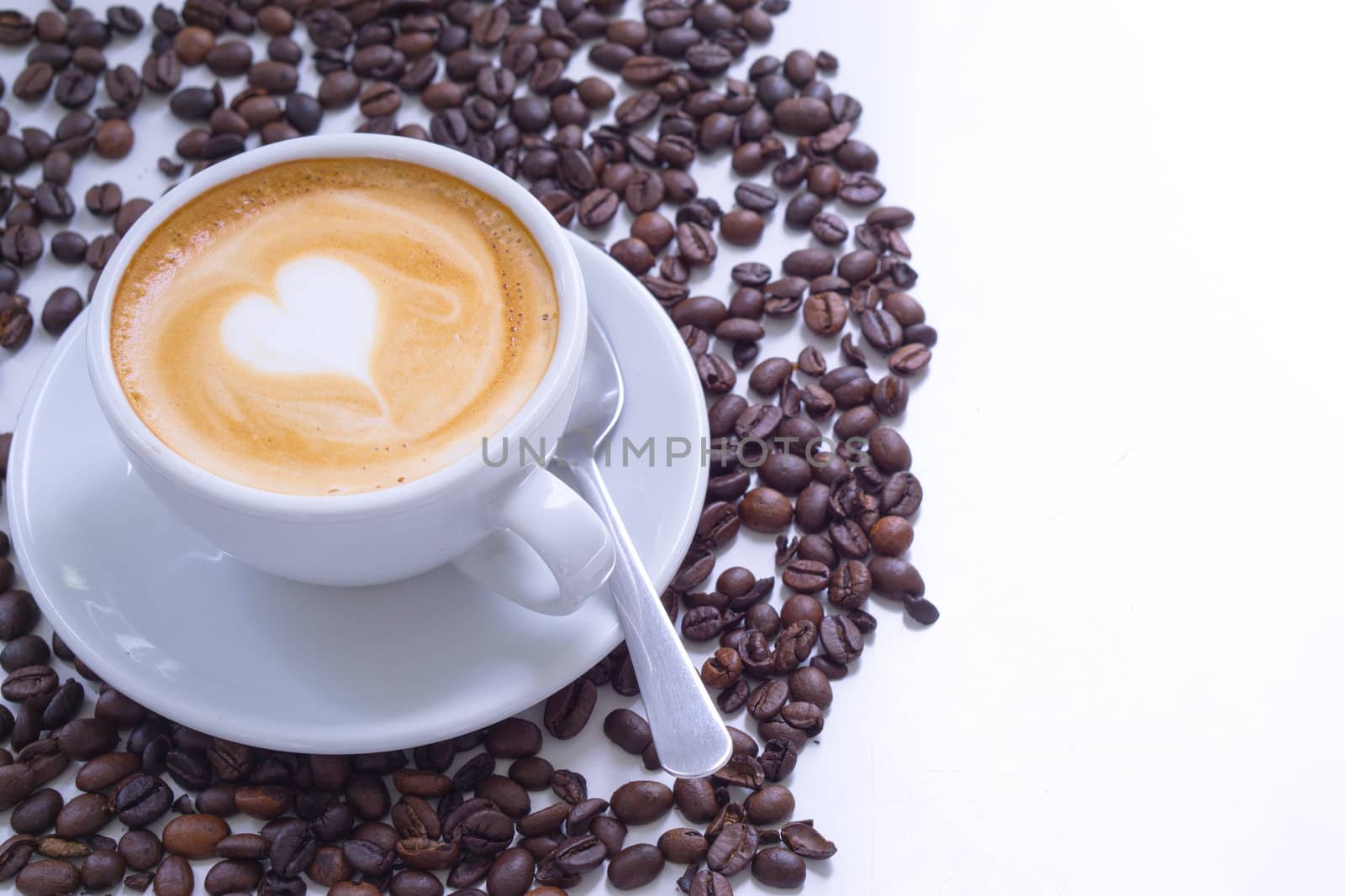 White cup of coffee latte with white heart shape milk foam and coffee beans on white table. top view, copy space for text.