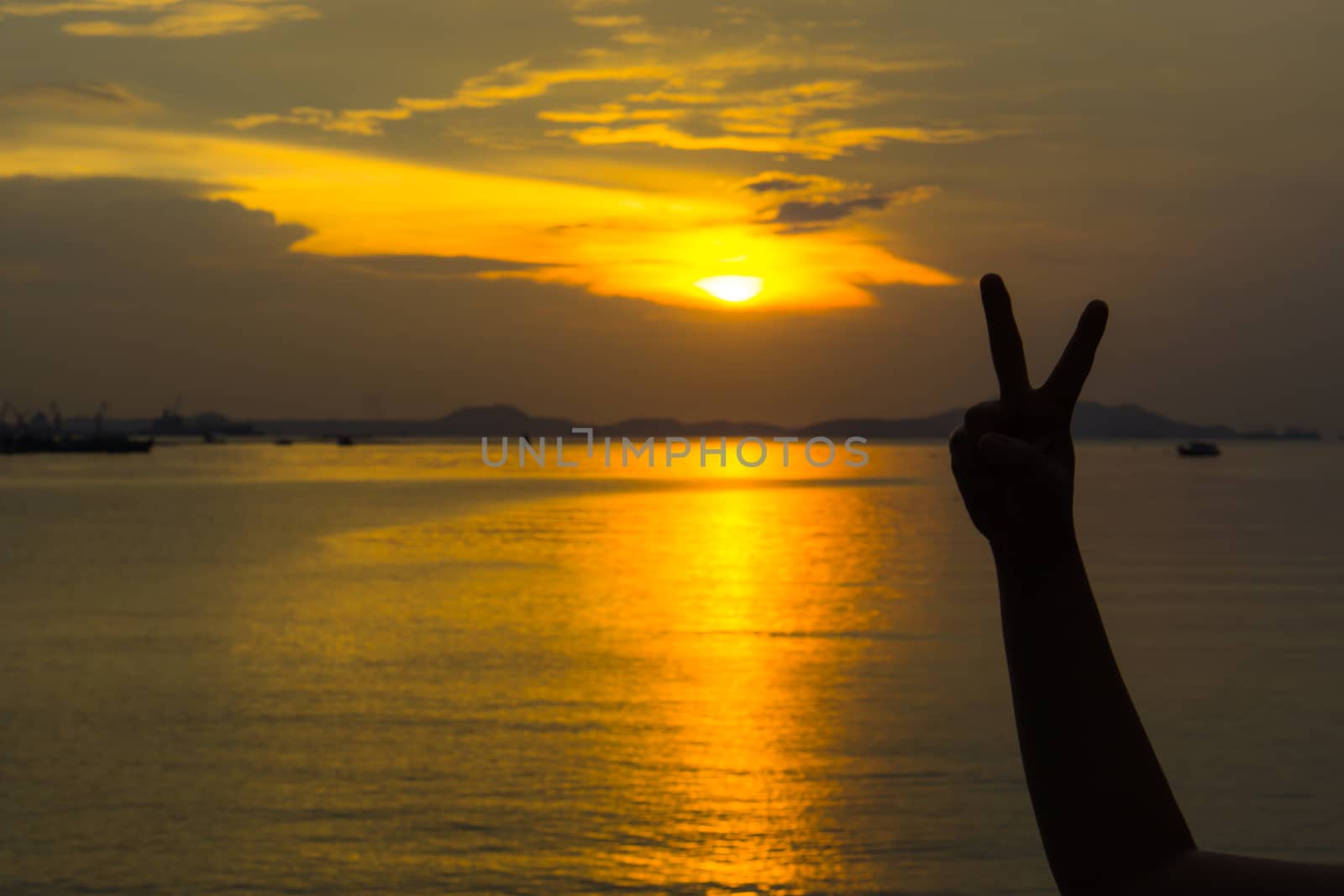 Silhouette of two fingers of woman's hand or victory in front of the sun during sunset time. Fighting concept