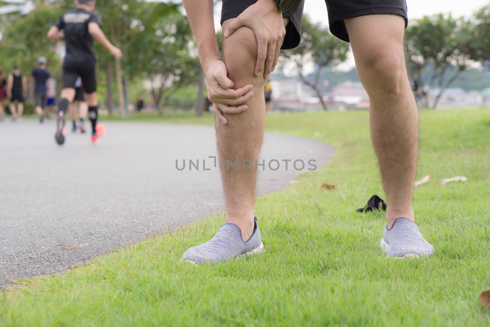 Knee Injuries. Young sport man holding knee with his hands in pain after suffering muscle injury during a running workout at park. Healthcare and sport concept.