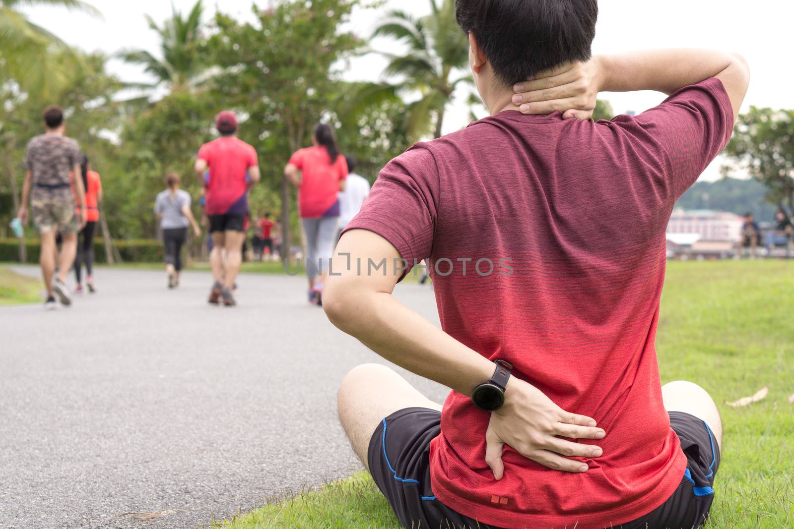 A male athlete suffering from neck and back pain and injury at the park. Sport and healthcare concept.