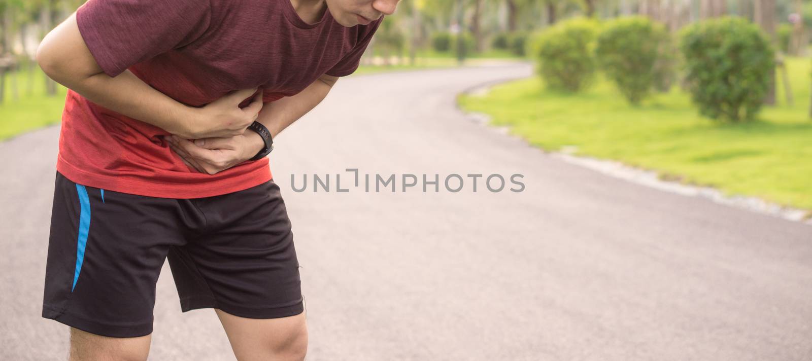 Sport man holding abdomen with his hands in stomach pain after running workout at park. Health care concept