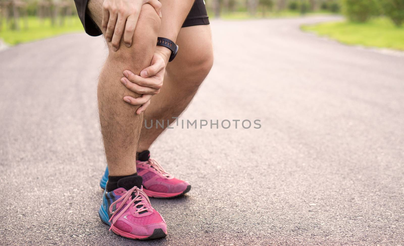 Knee Injuries. Young sport man holding knee with his hands in pain after suffering muscle injury during a running workout at park. Healthcare and sport concept.