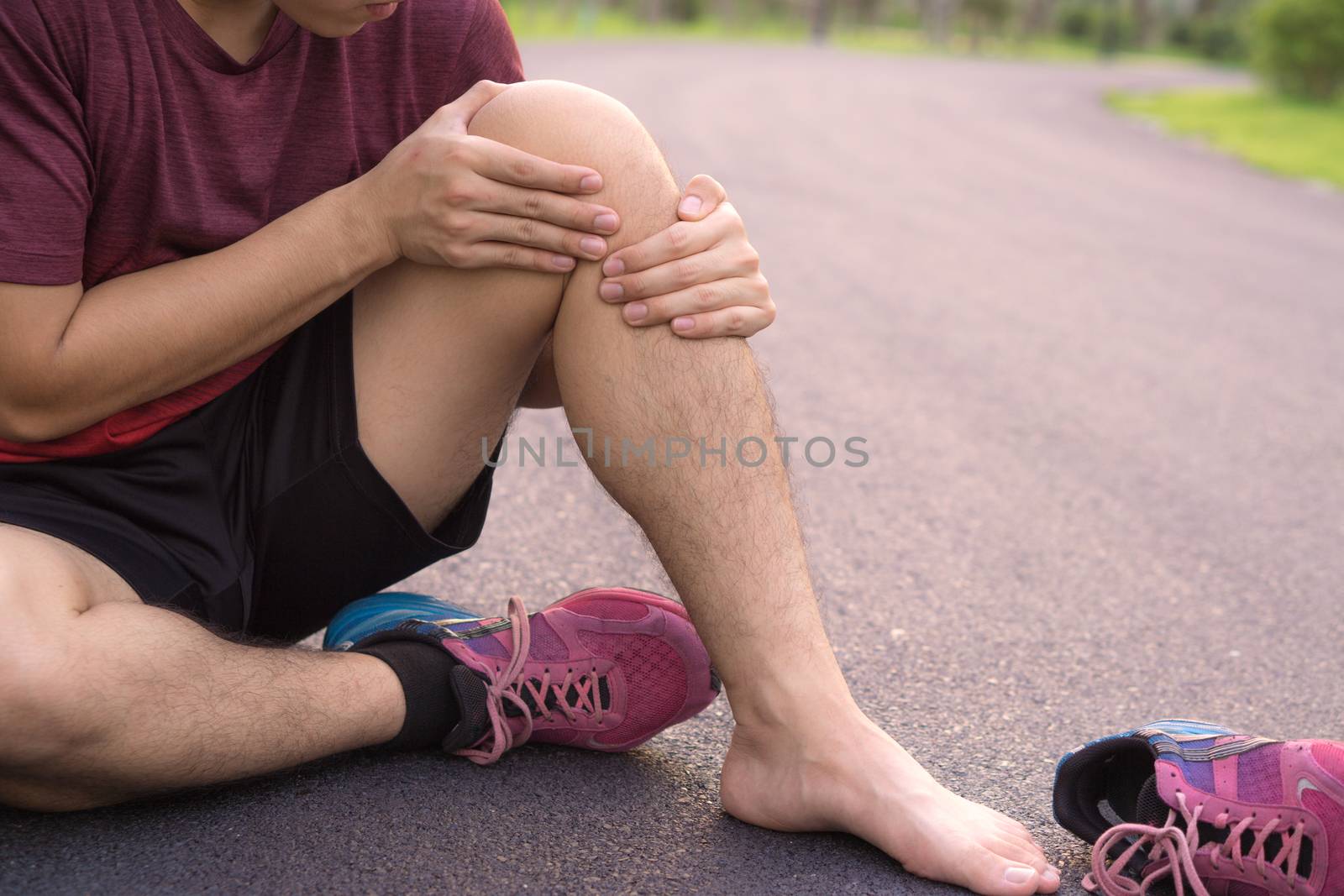 Knee Injuries. Young sport man holding knee with his hands in pain after suffering muscle injury during a running workout at park. Healthcare and sport concept.