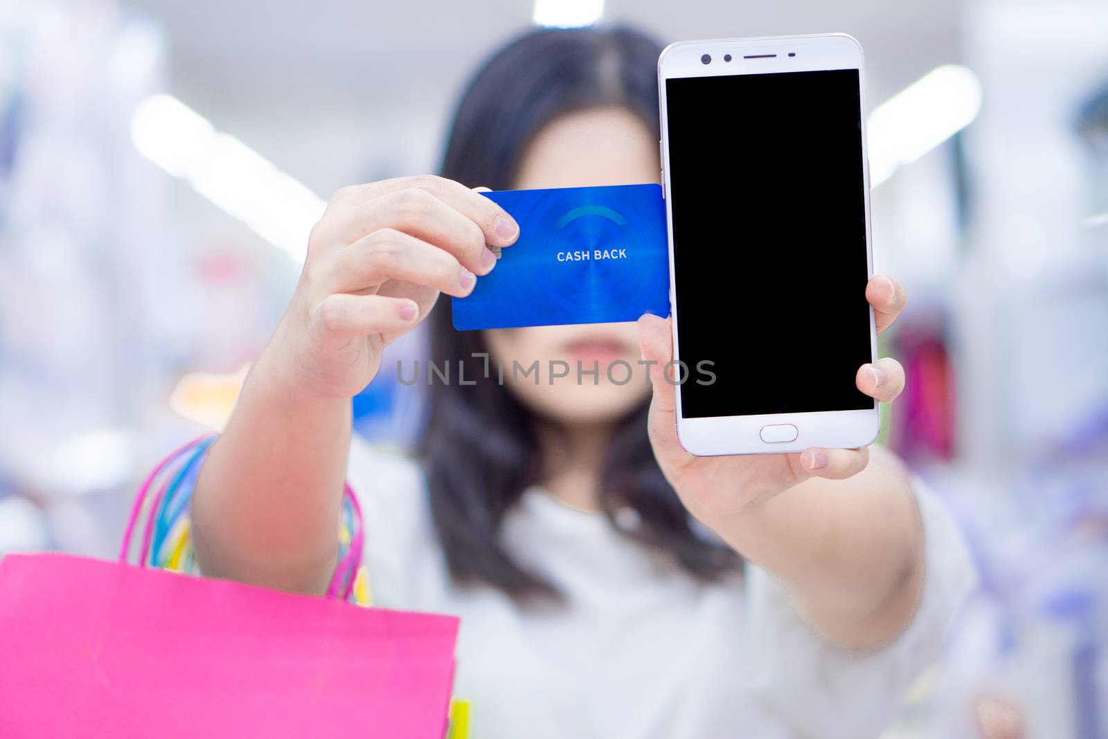 Close up woman hand holding phone, shopping bag and credit card in the shopping mall. Shopping concept.