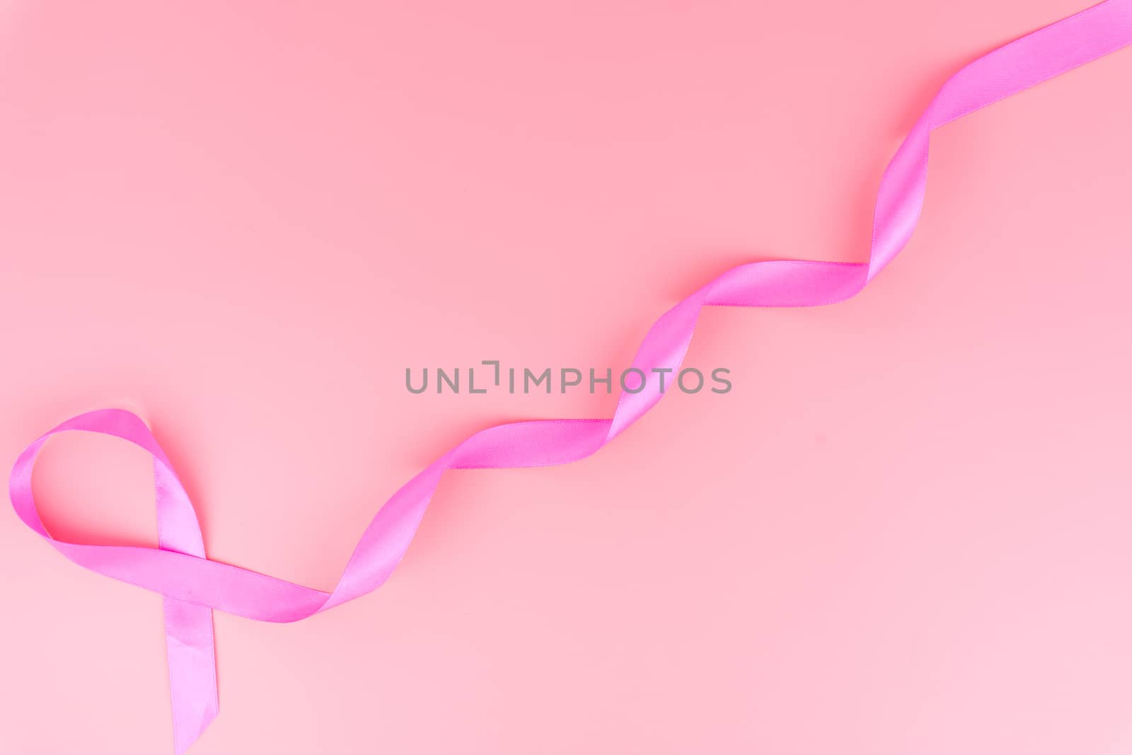 Pink ribbon breast cancer on pink background with copy space for text. Flat lay, top view.