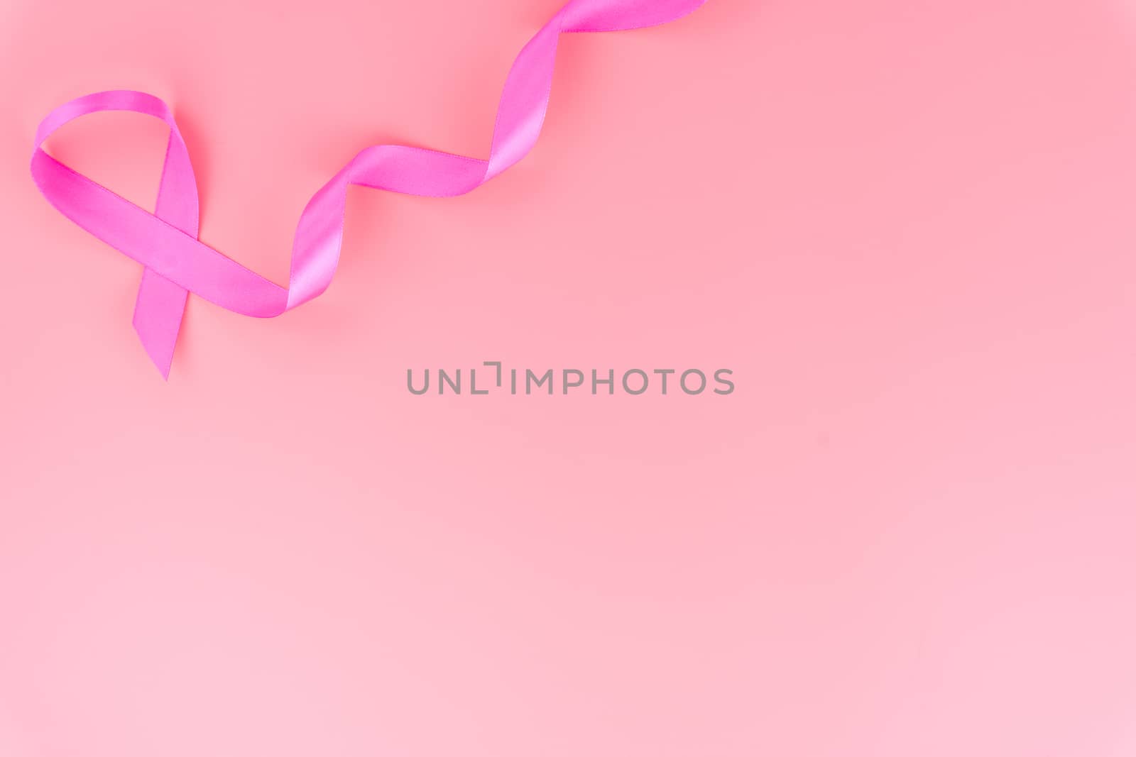 Pink ribbon breast cancer on pink background with copy space for text. Flat lay, top view.