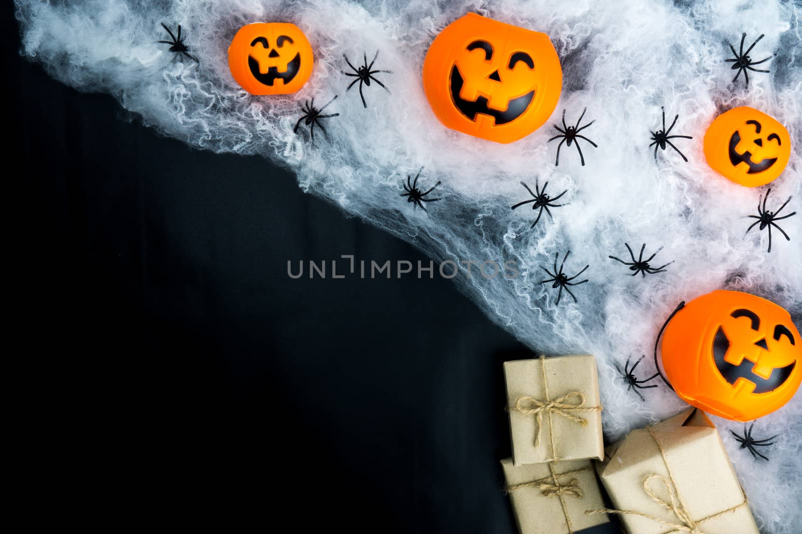 Halloween holiday background with spider, webs, gifts and jack lantern on black background with copy space for text. Flat lay, top view