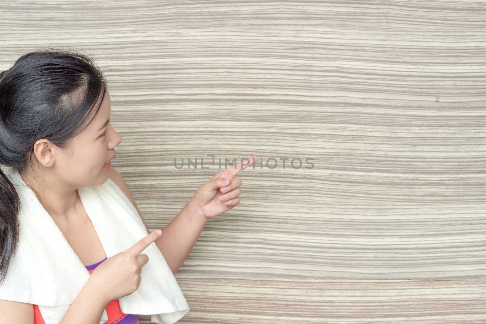 Young woman standing and pointing finger at copy space wooden background at fitness gym. Shows free space for your promotional.