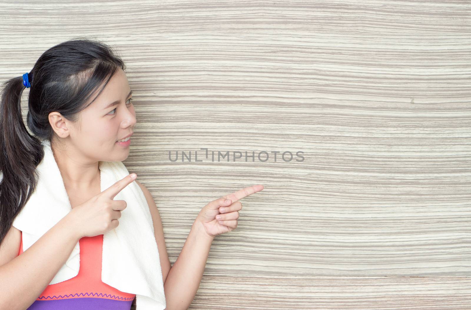 Young woman standing and pointing finger at copy space wooden background at fitness gym. Shows free space for your promotional.