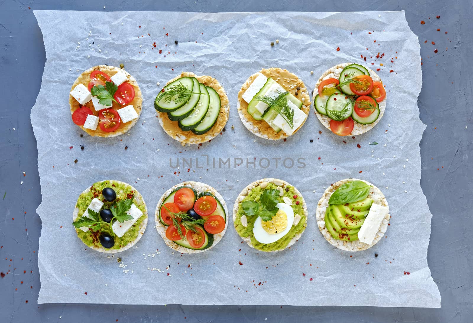 Assorted tasty appetizers with fresh vegetables, feta cheese and egg on crumpled paper viewed from overhead in two neat rows