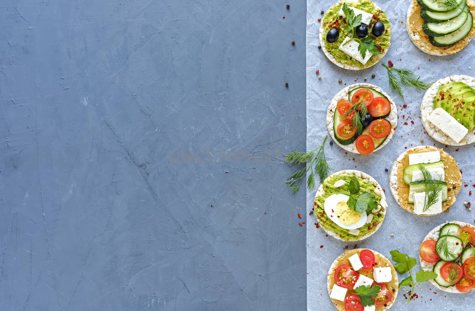 Selection of savory appetizers with fresh vegetables, cheese and herbs arranged as a border on a blue background with copy space