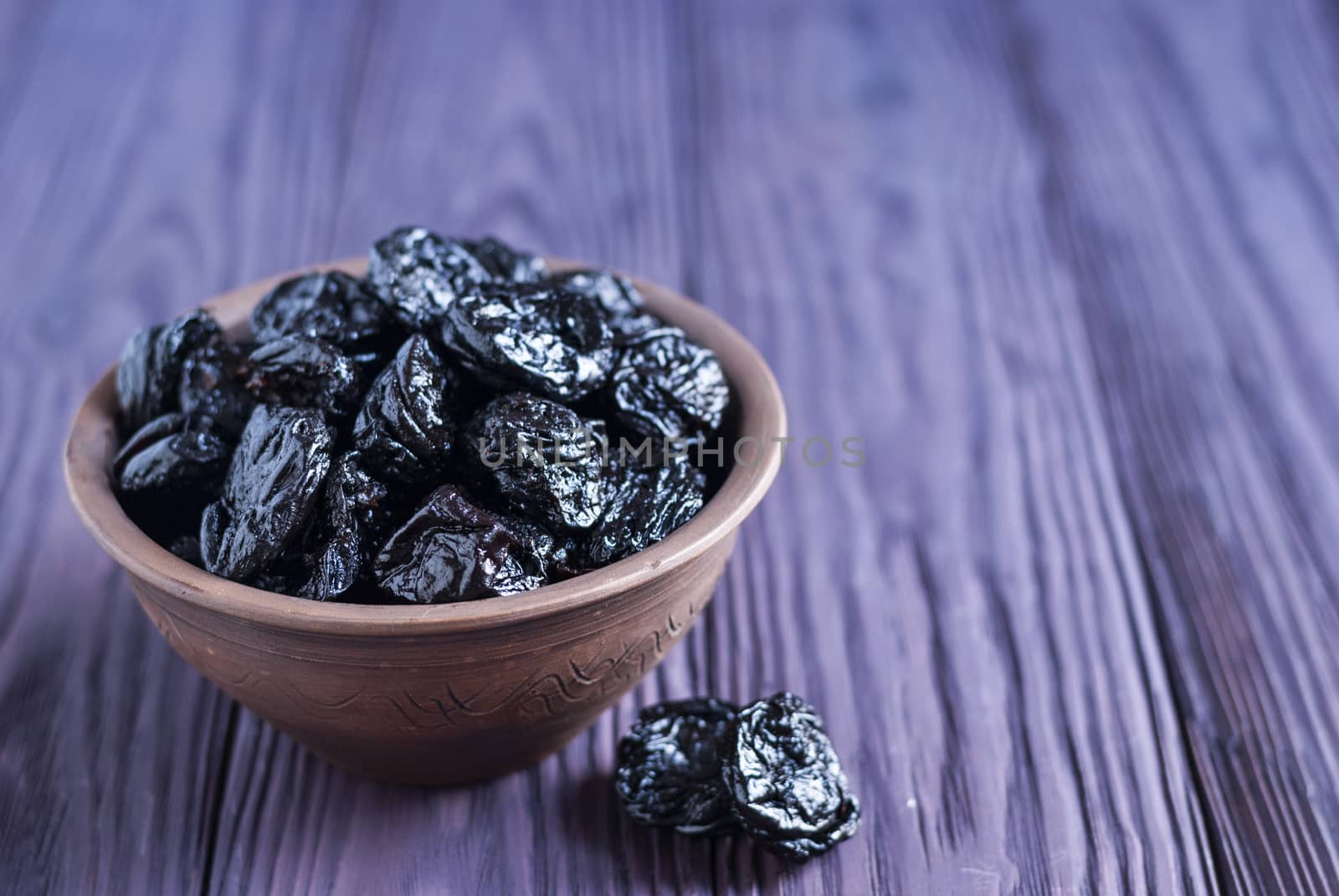 Closeup of clay bowl filled with shiny sweet prunes on wooden table