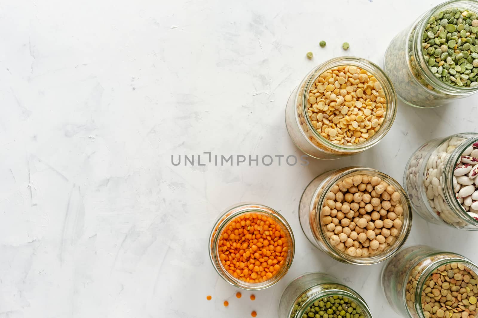 Colorful healthy dried legumes in glass jars over a textured white background with copy space viewed from overhead