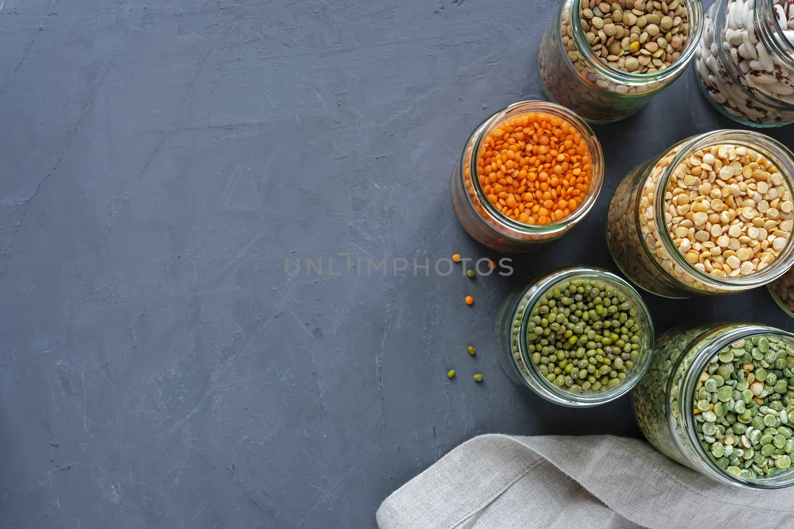 Dried legumes in storage jars on mottled blue background viewed from above with lentils, peas, and beans and copy space