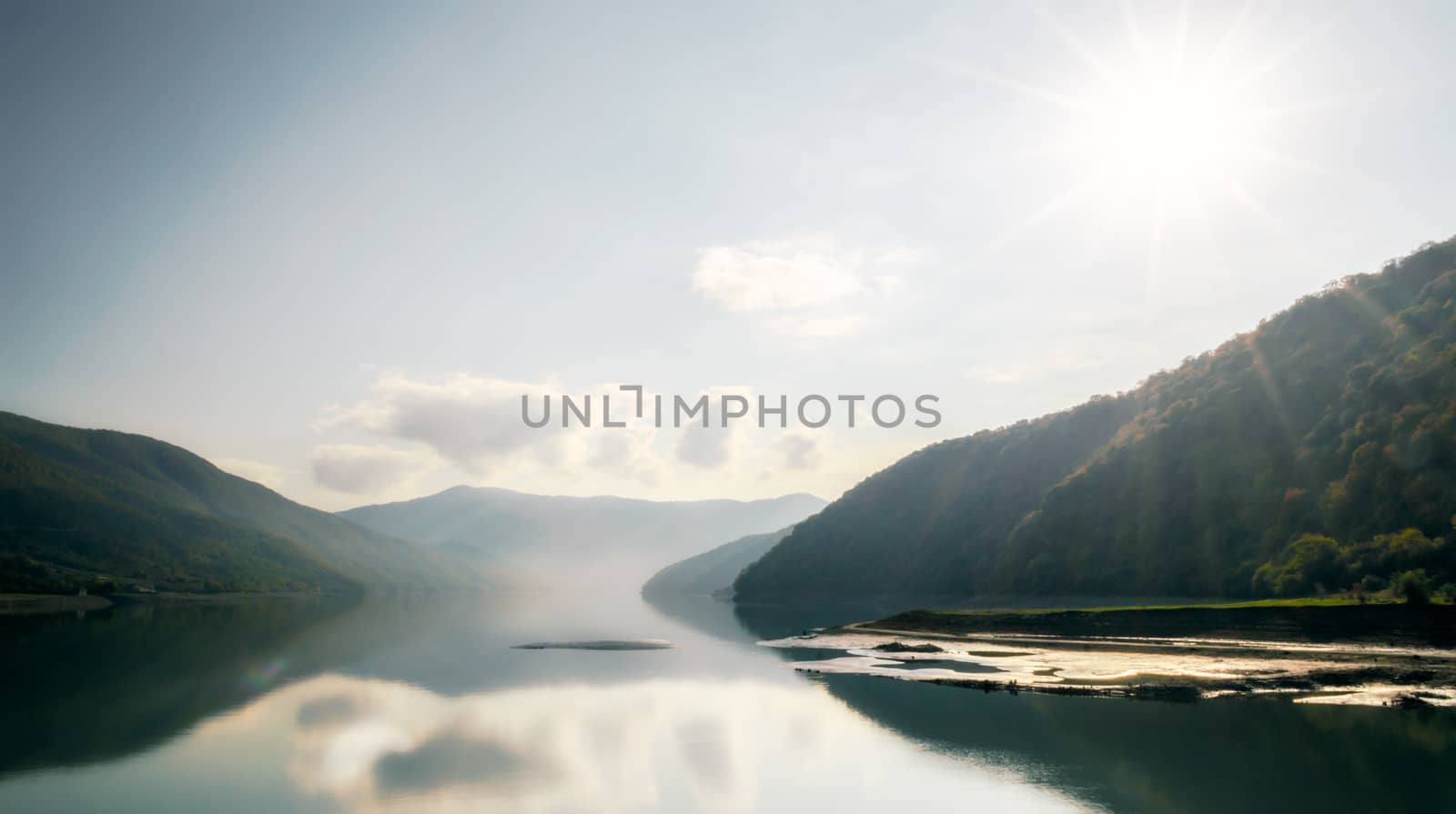 autumn mountain landscape with green forest and lake against the background of the rays of the sun and sky and clouds in Georgia