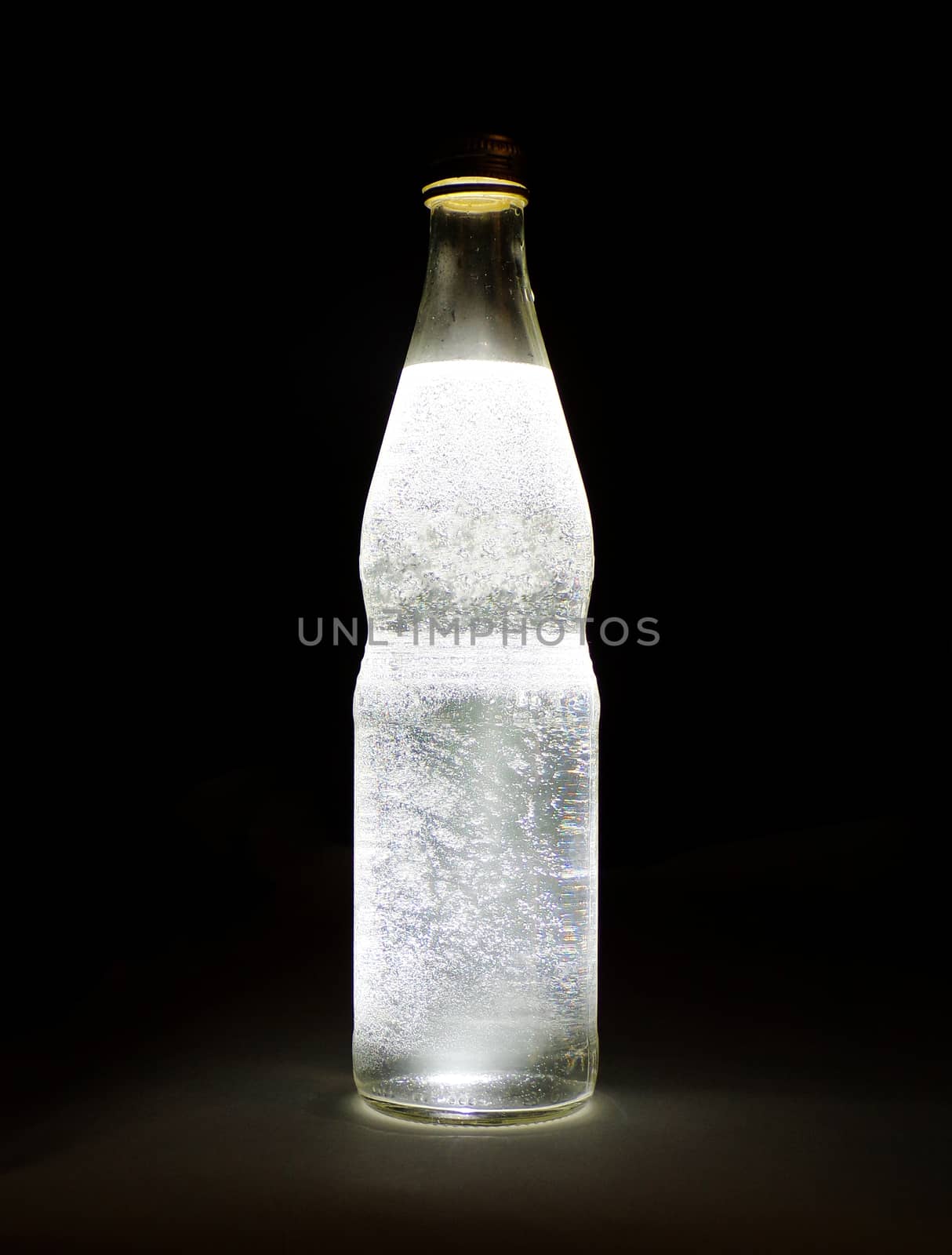 Cold mineral water with gas bubbles on a black background. Beautiful glass bottle close-up.