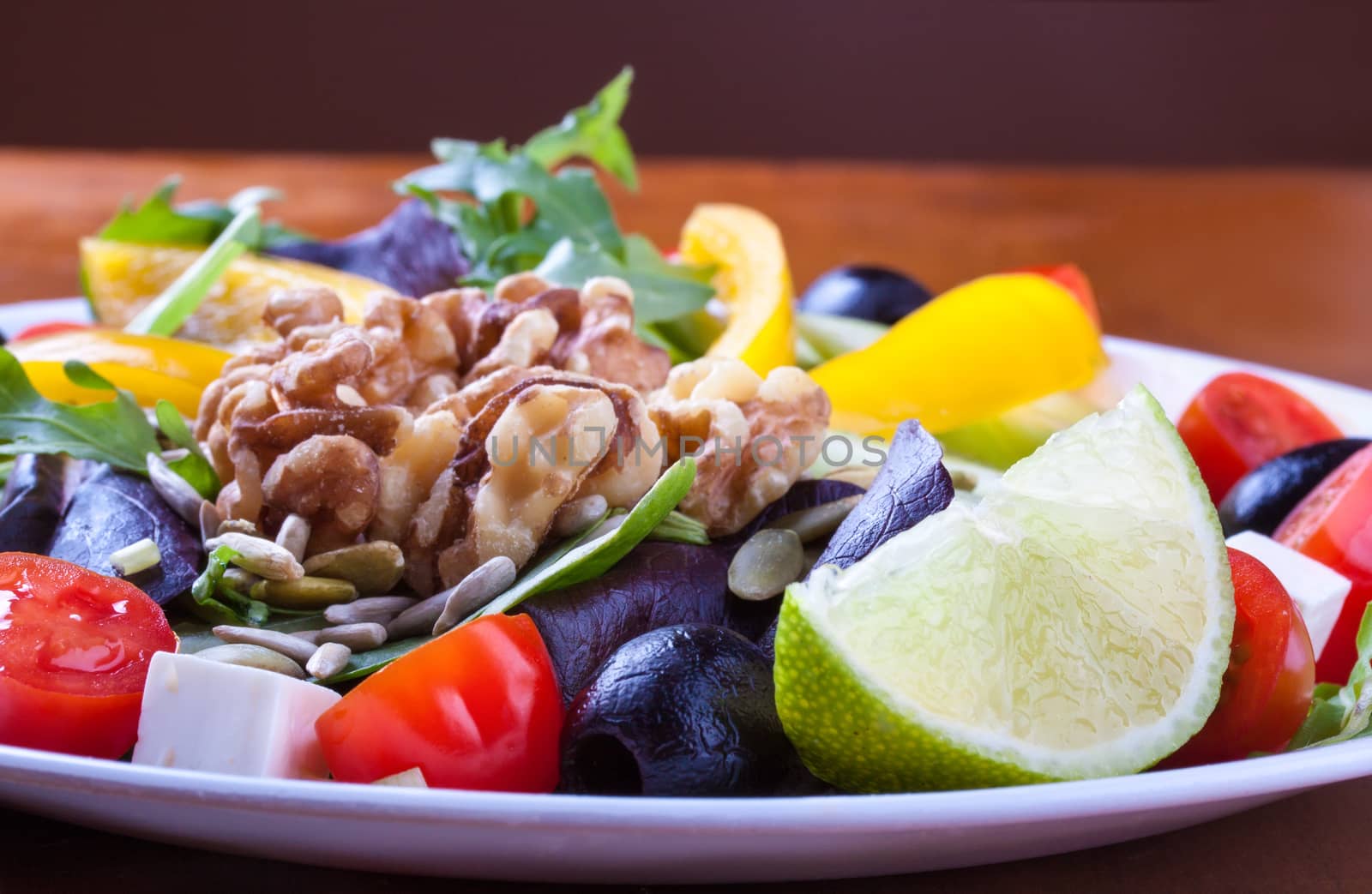 Closeup on a fresh healthy green salad with olive, cheese and walnuts in a white plate