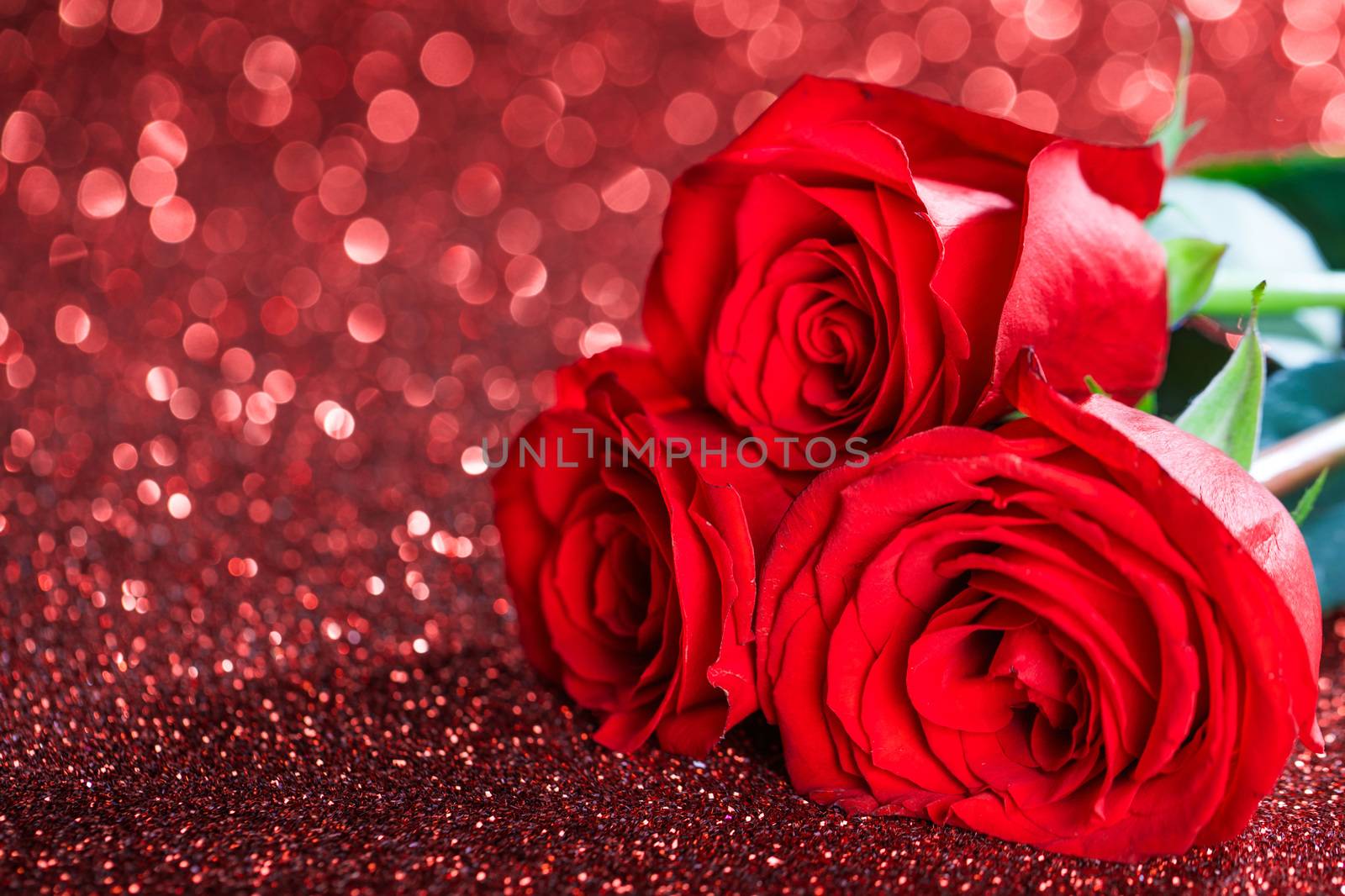 Three red roses over bokeh glittering background