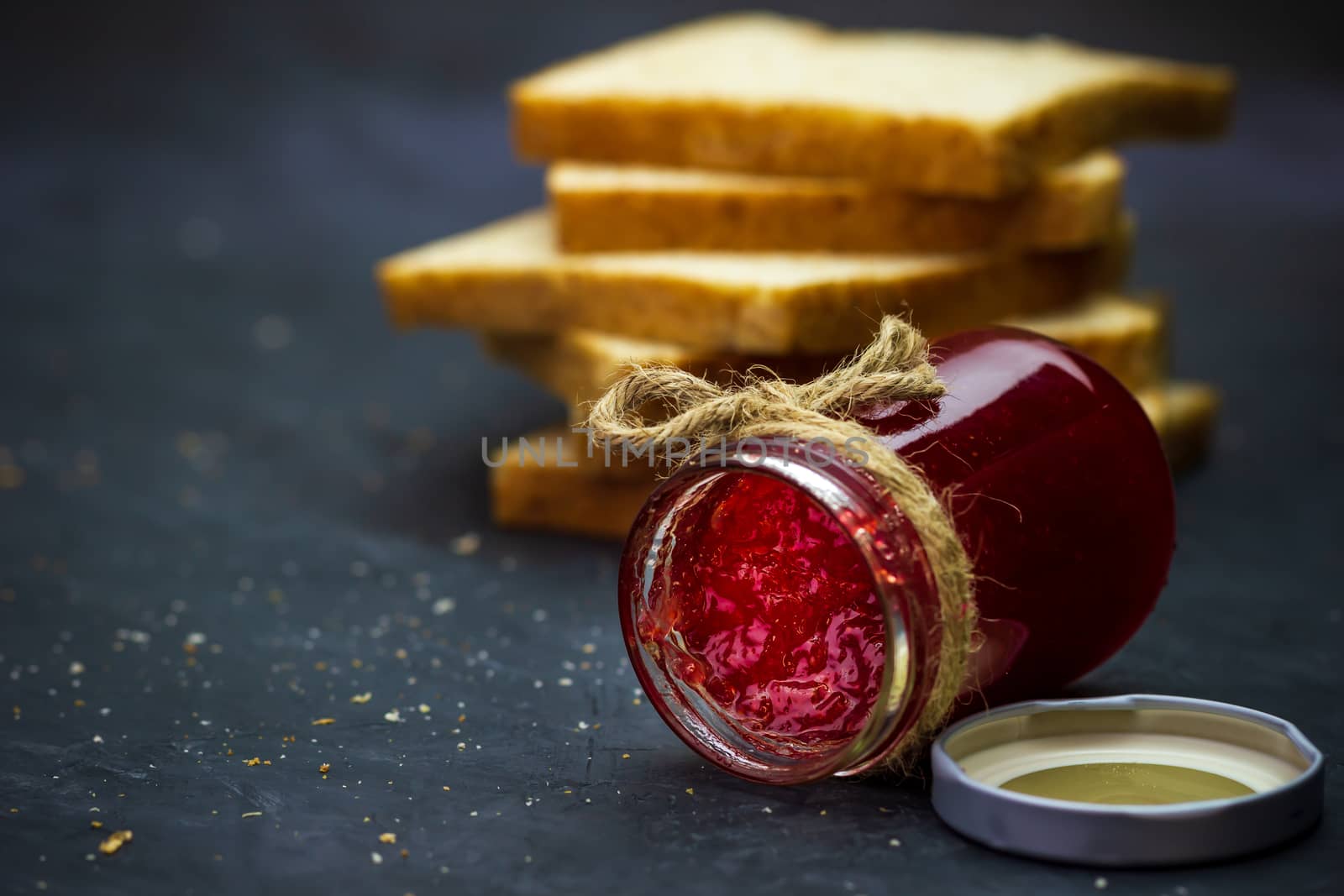 Strawberry jam bottle and whole wheat bread are stacked on a black background. Concept of breakfast and healthy food.