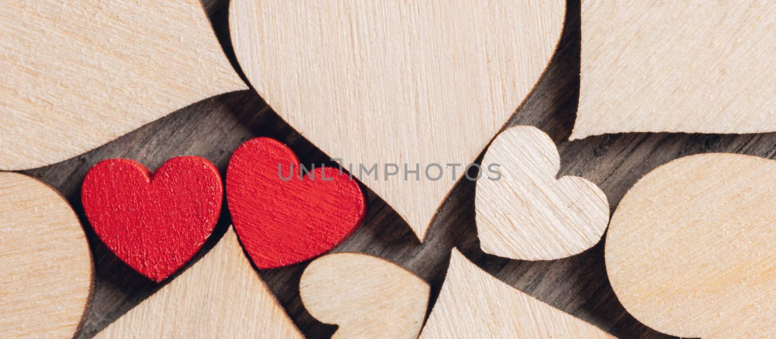 Two wooden painted red hearts among many colorless wooden hearts