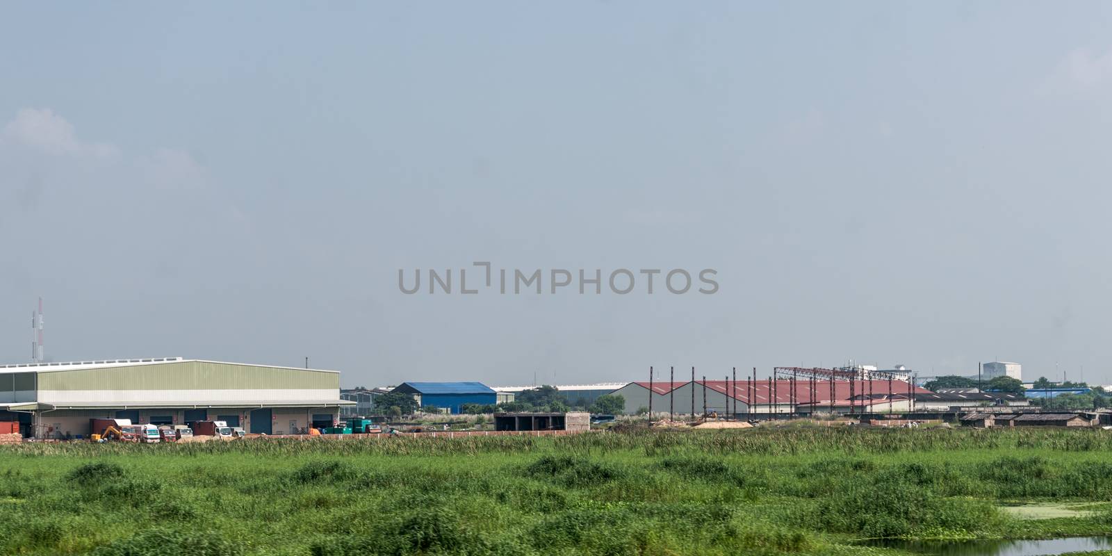 Industrial site power plant landscape. Industry surrounded by rural agricultural field and green summer meadow. A beautiful non-urban scenic environment of Rural Countryside of India, south asia pac. by sudiptabhowmick