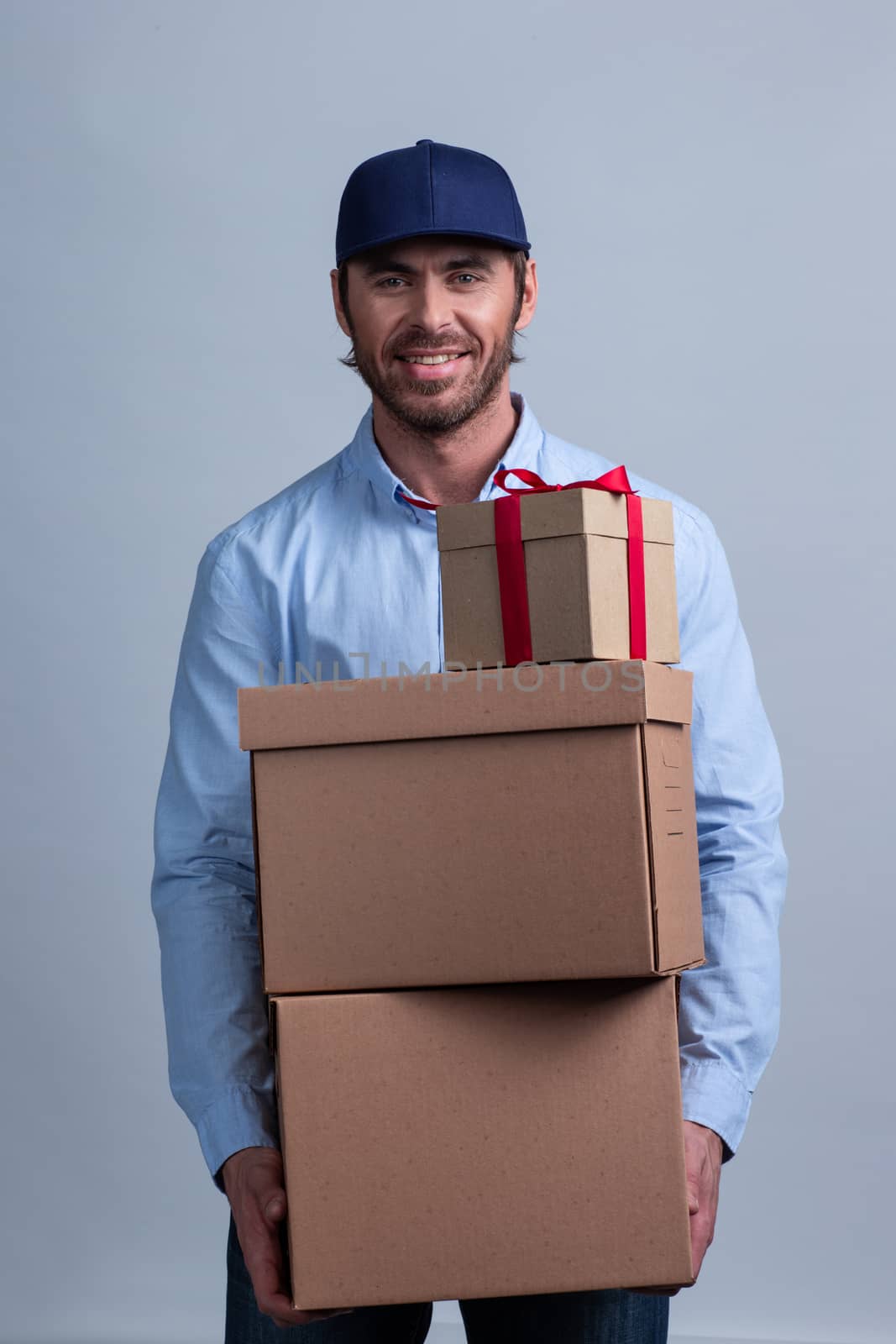 Happy smiling delivery man in uniform cap holding box stack