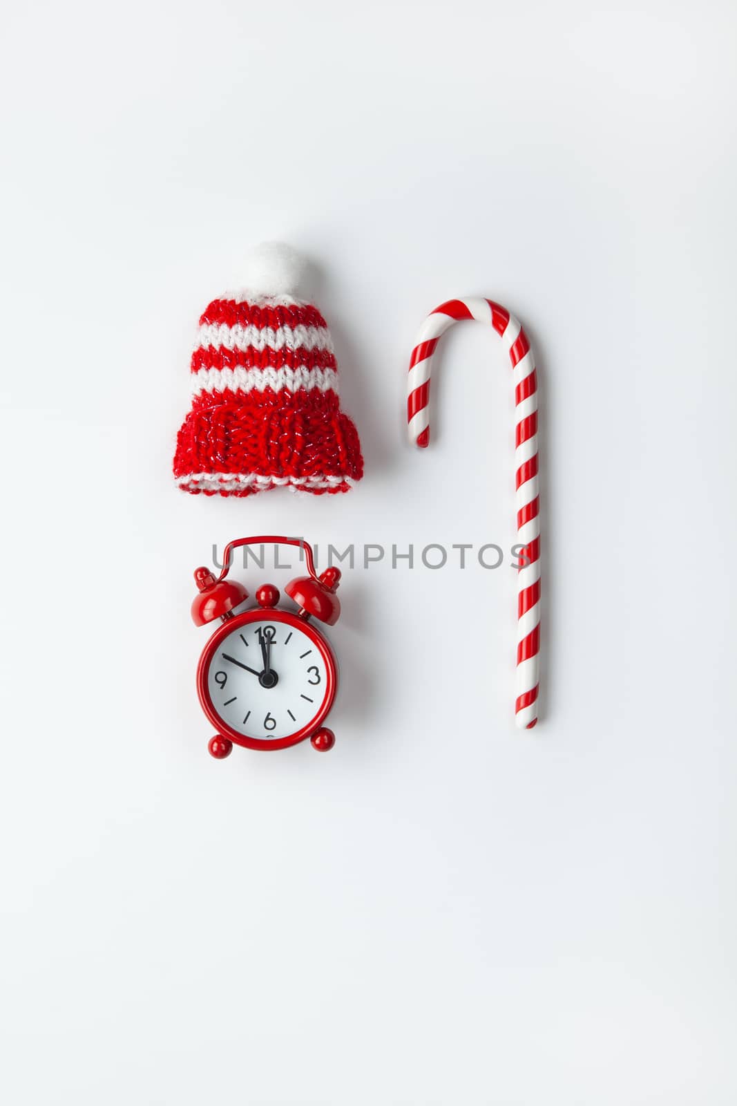 Christmas composition, cane candy, small analog clock, striped hat on white background. Minimal style. Top view. Festive, holiday concept. For social media, greeting card.