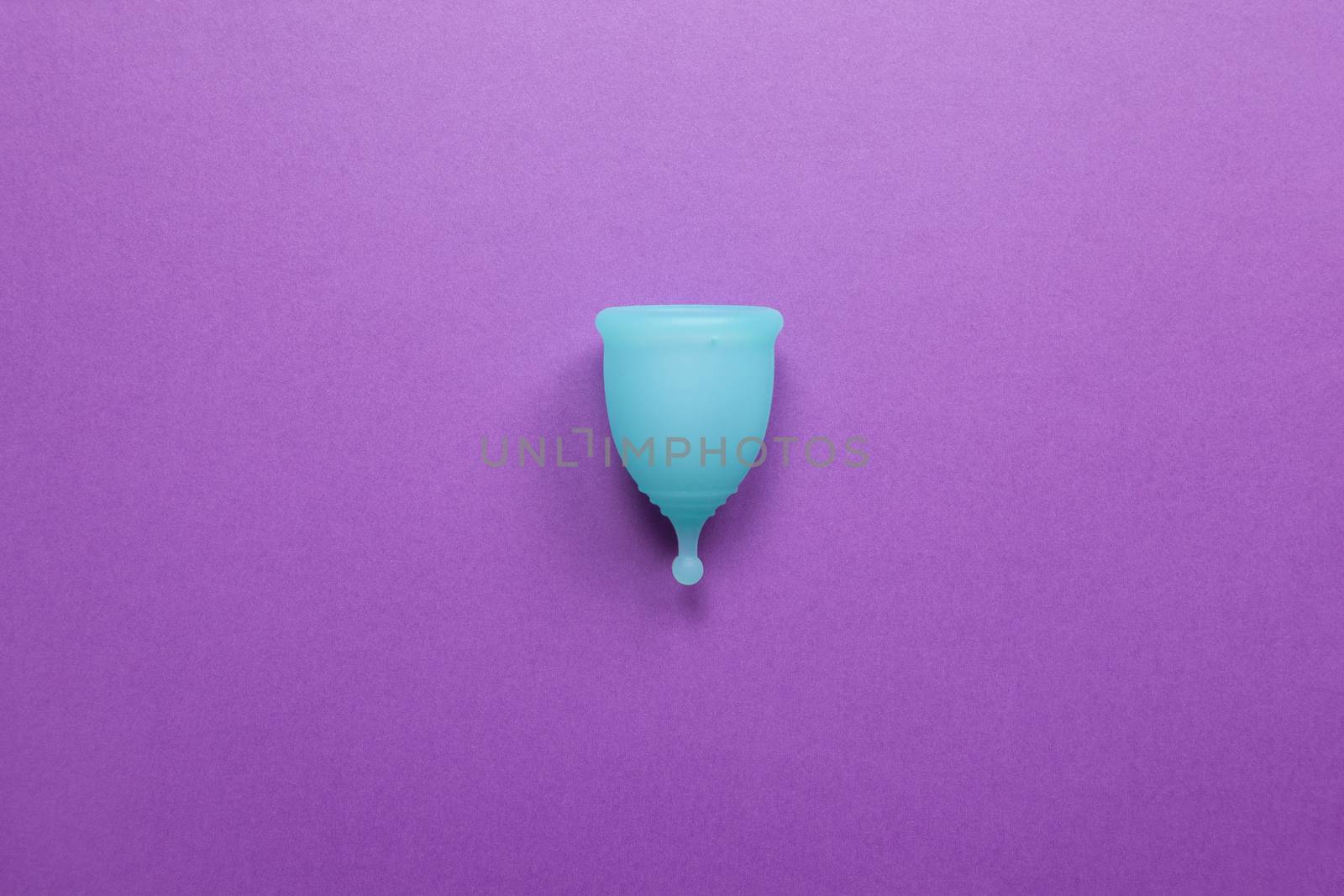 Turquoise menstrual cup on purple background. Concept zero waste living, savings, minimalism, these days. Feminine hygiene product, flat lay, copy space. Horizontal.