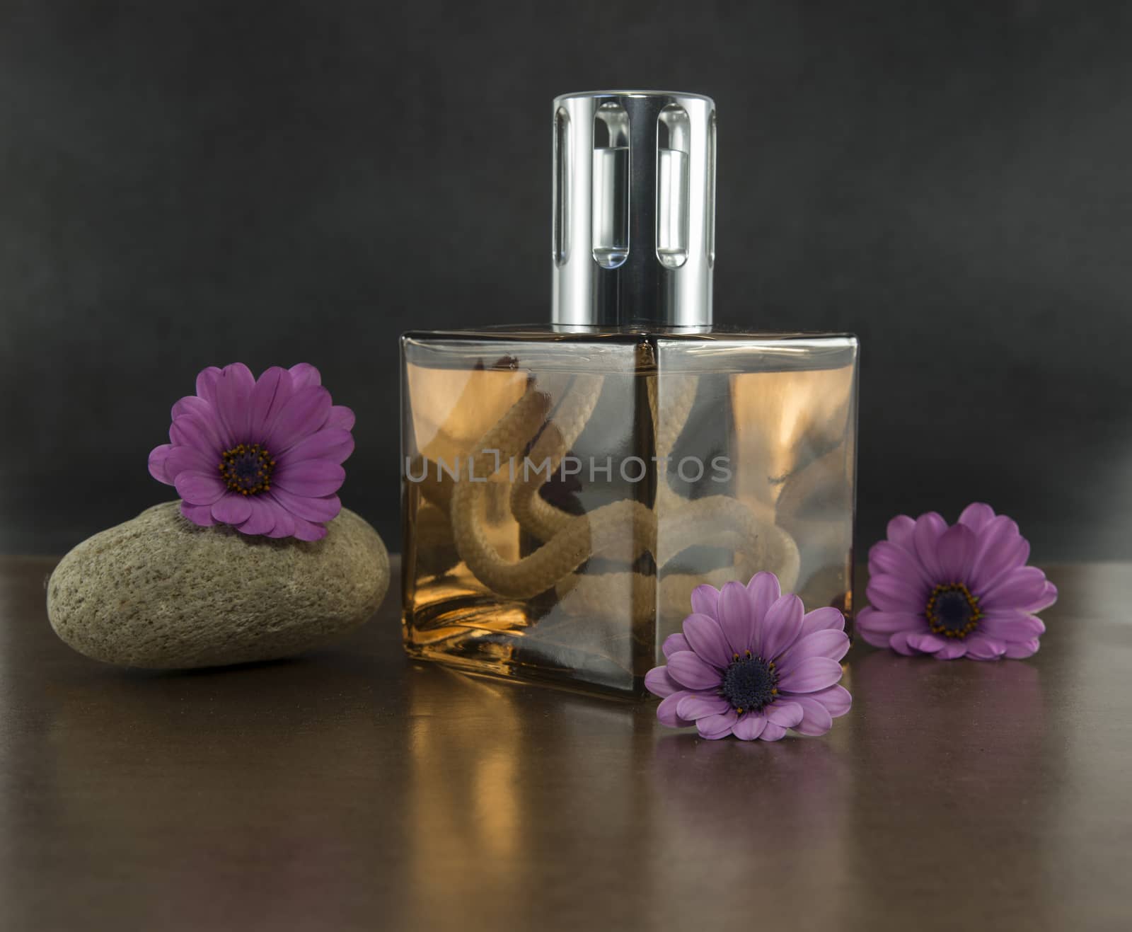 exclusive golden coloured parfum in glass bottle woth ze setting with spanish daisy flowers and stackes stones on dark background