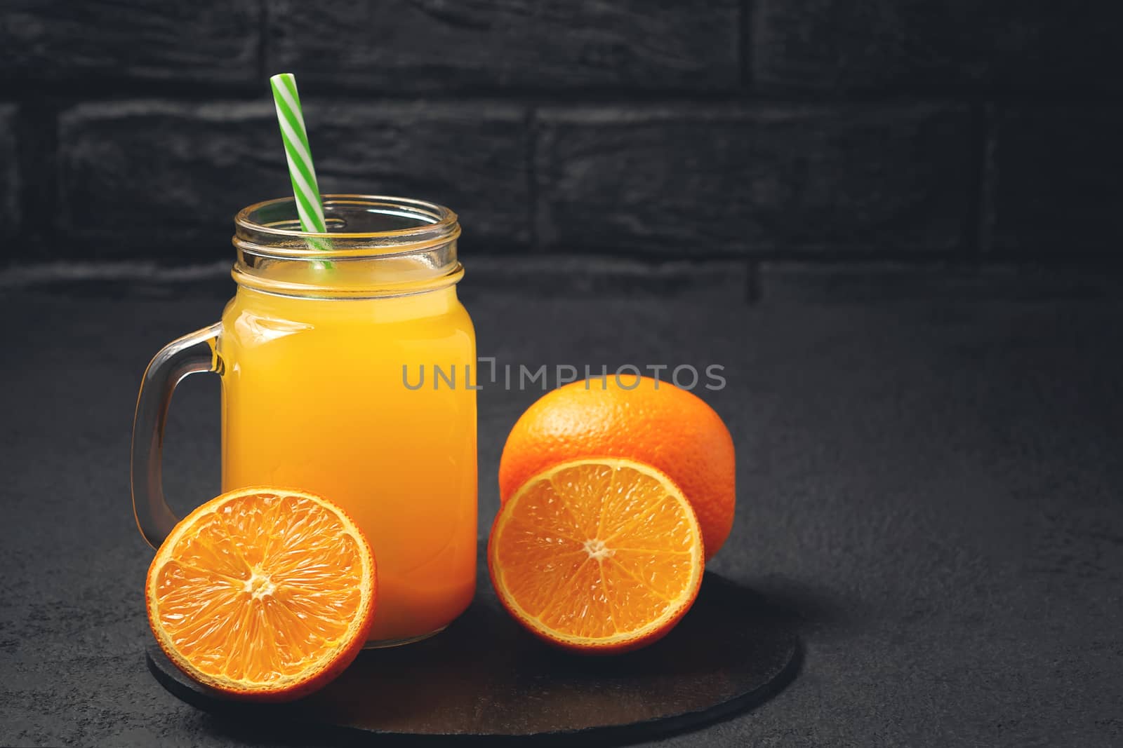 Homemade freshly squeezed orange juice in a Masonic jar and oranges on a black background, copyspace by galsand