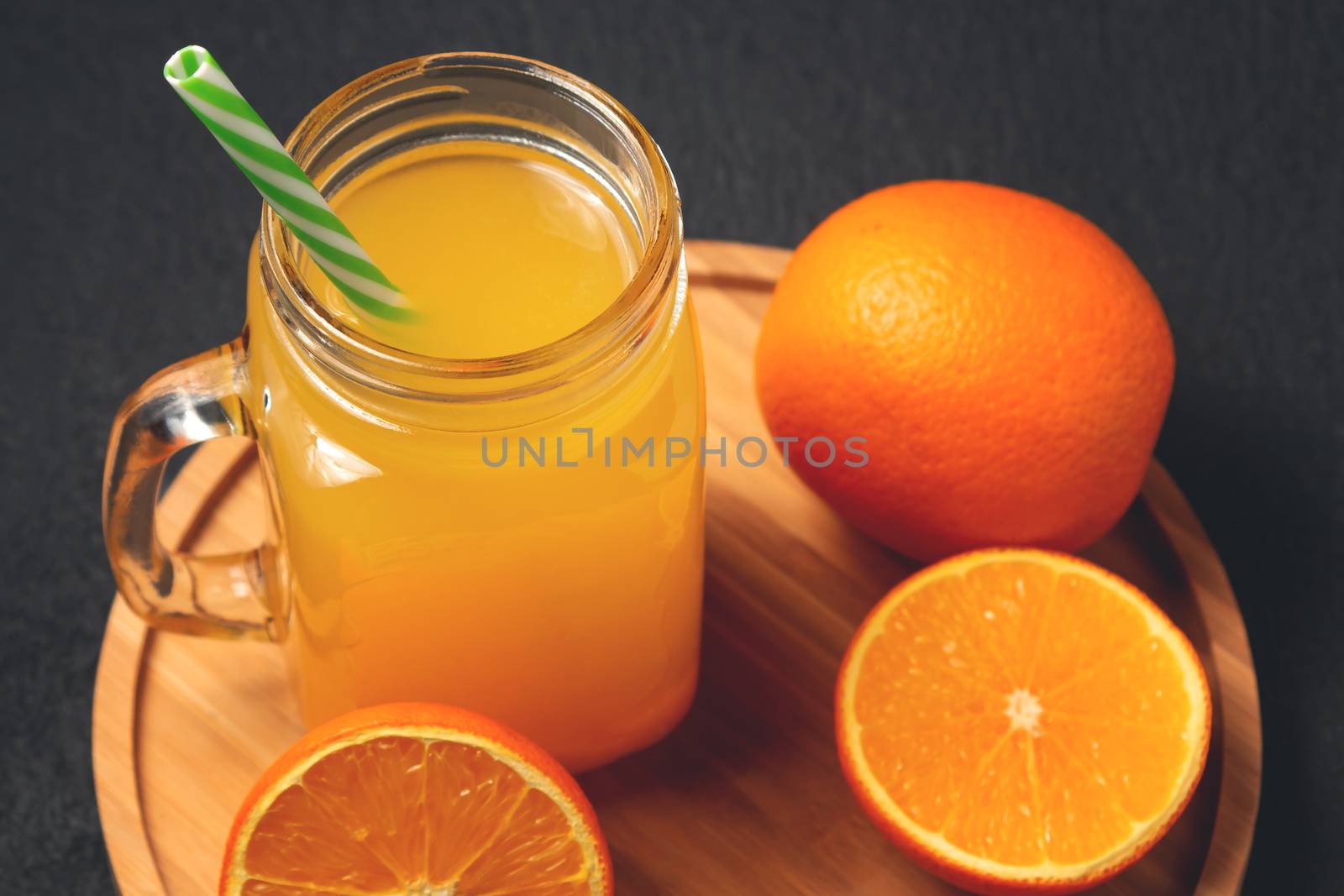 Homemade freshly squeezed orange juice in a mason jar and oranges on wooden dish on a black background.