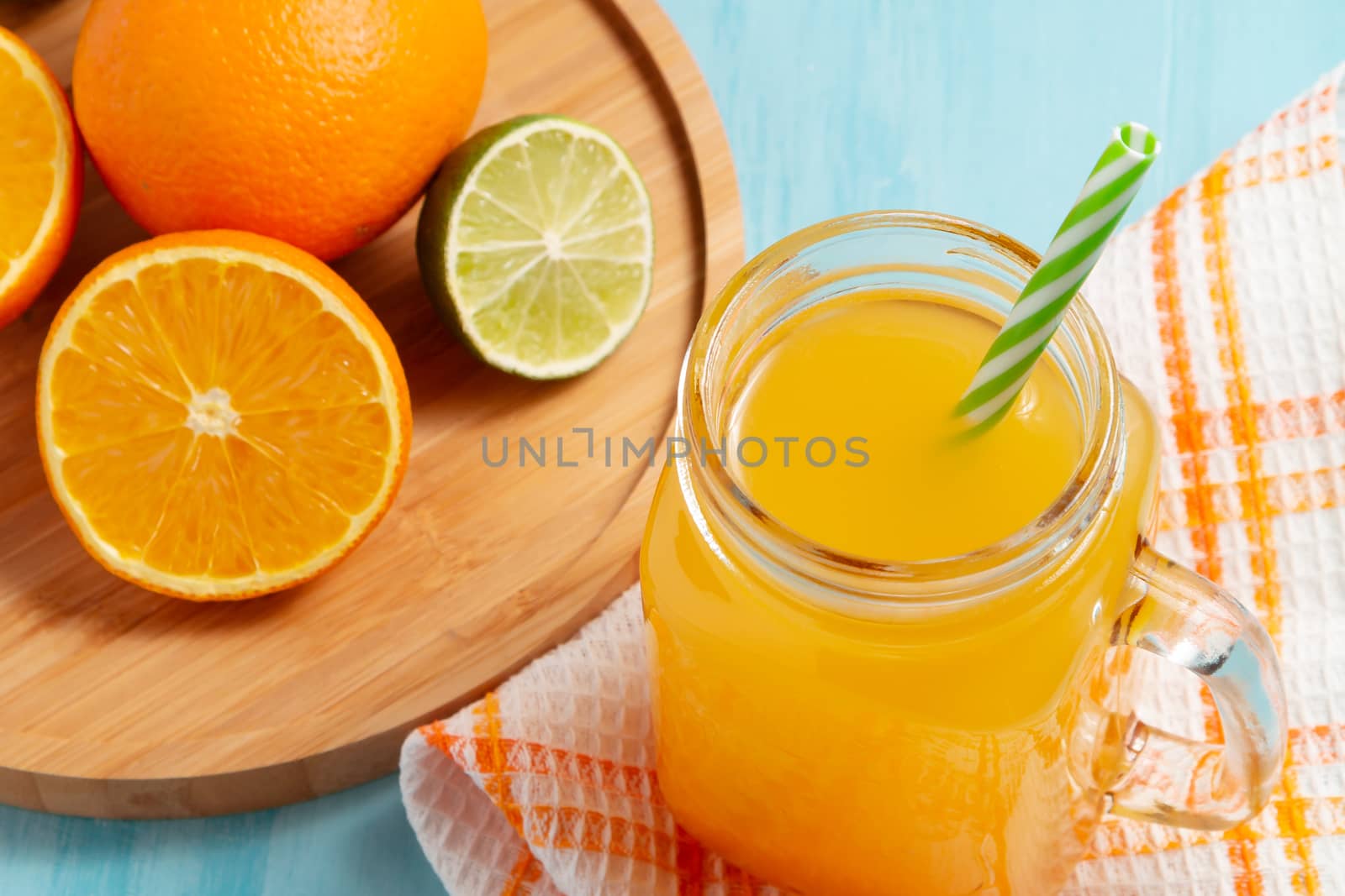 Homemade freshly squeezed orange juice in a mason jar, oranges and lime on wooden dish closeup.