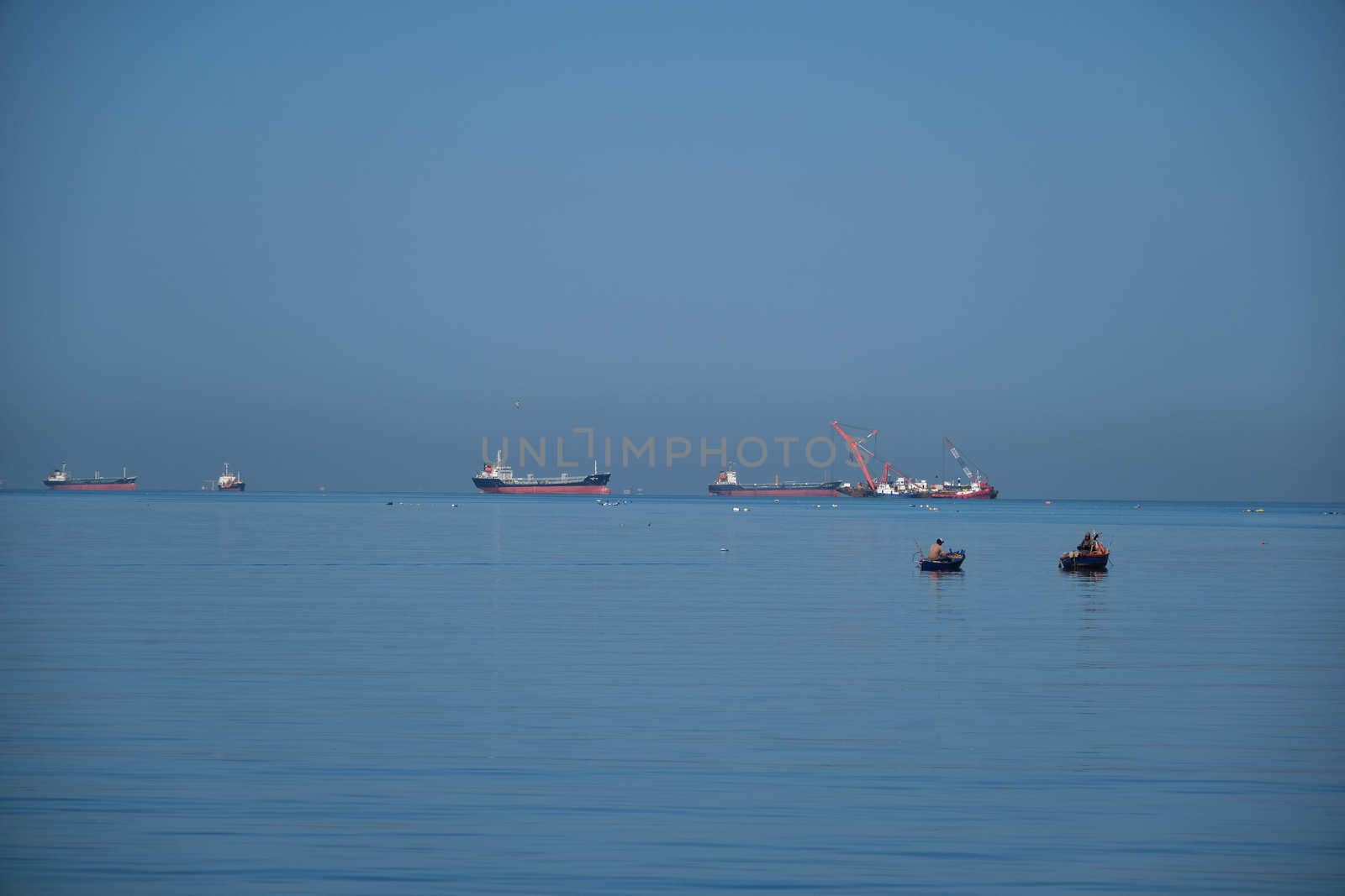 The Small Fisherman Boat in the Sea. A small fisherman boat floating on the sea near the seashore with Cargo ship background