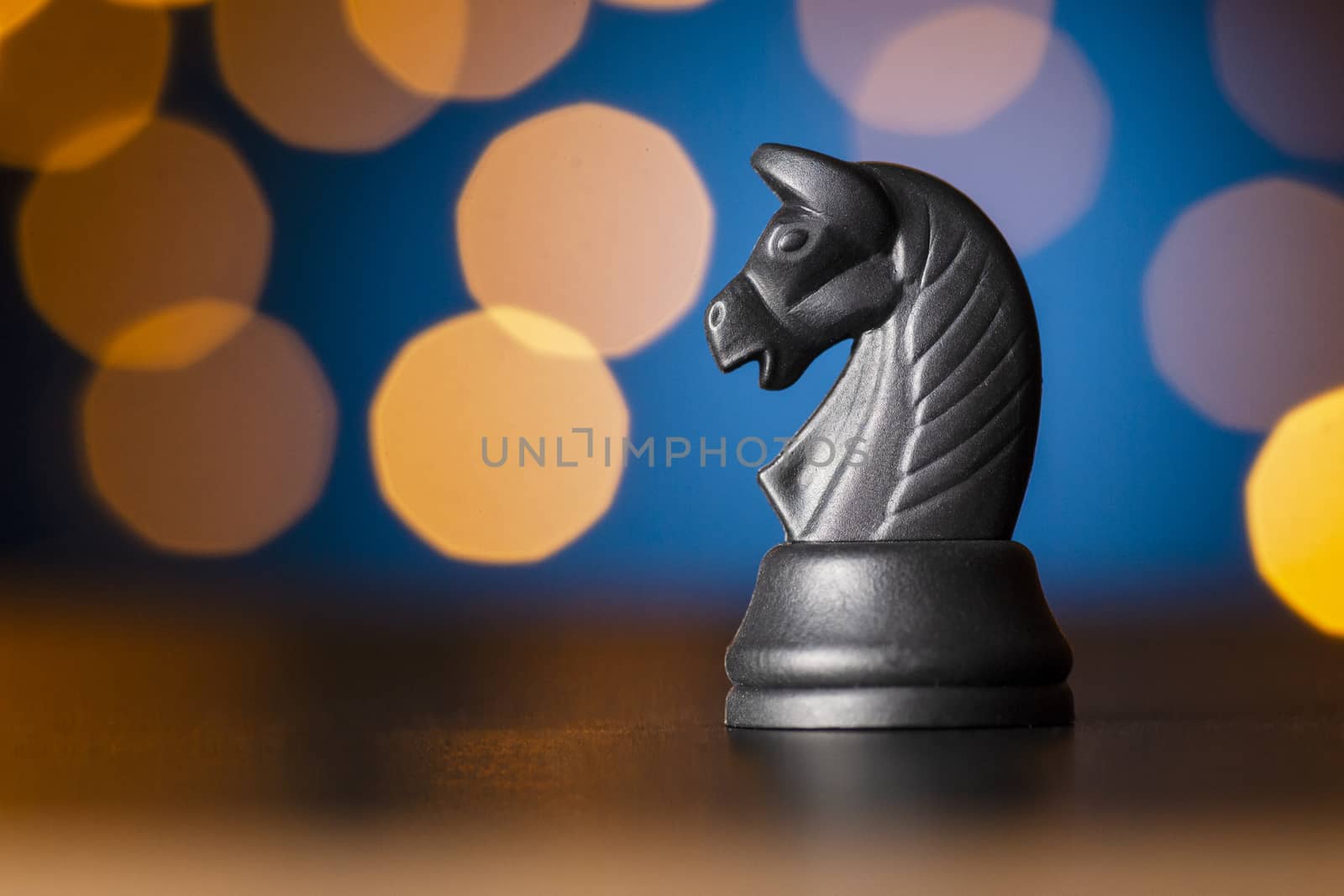 black horse chess piece on a wooden table over a colorful bokeh effect of golden light in a conceptual image