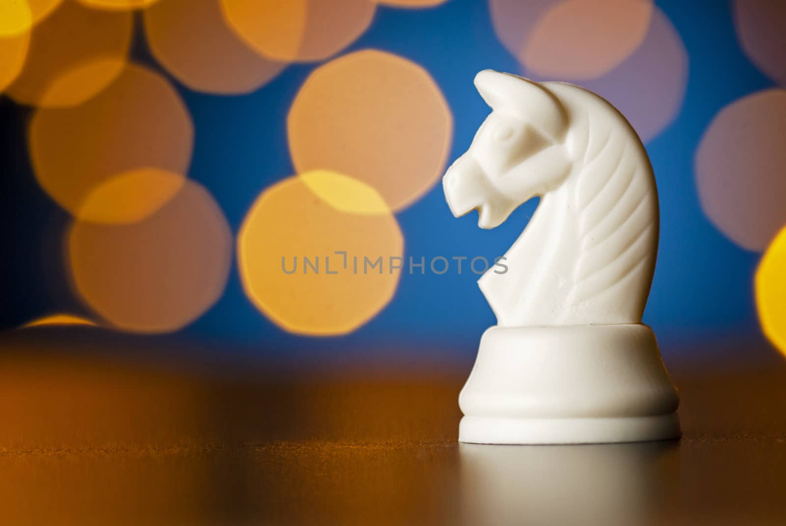 White horse chess piece on a wooden table over a colorful bokeh effect of golden light in a conceptual image