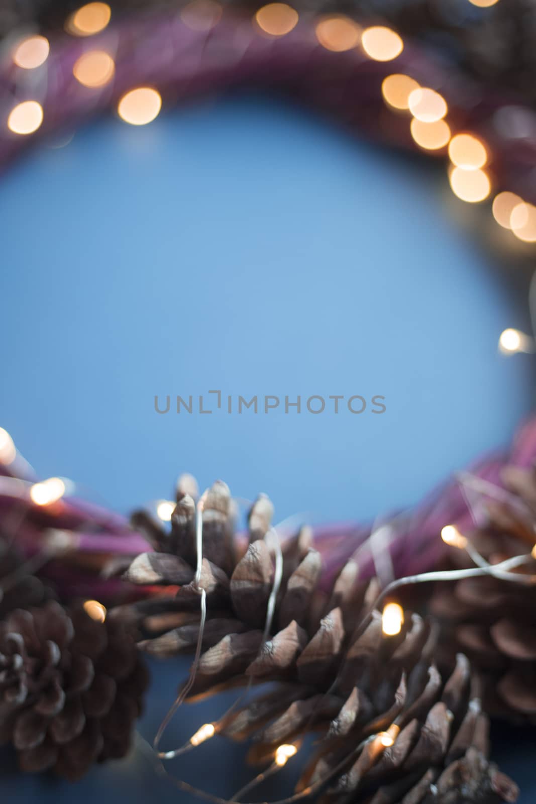 Christmas wreath of pine cones and glowing lights garland on blue background copy space text