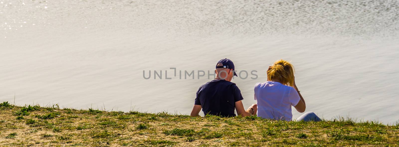 male and female couple sitting at the water side of tholen beach, Bergse diepsluis, Zeeland, The netherlands