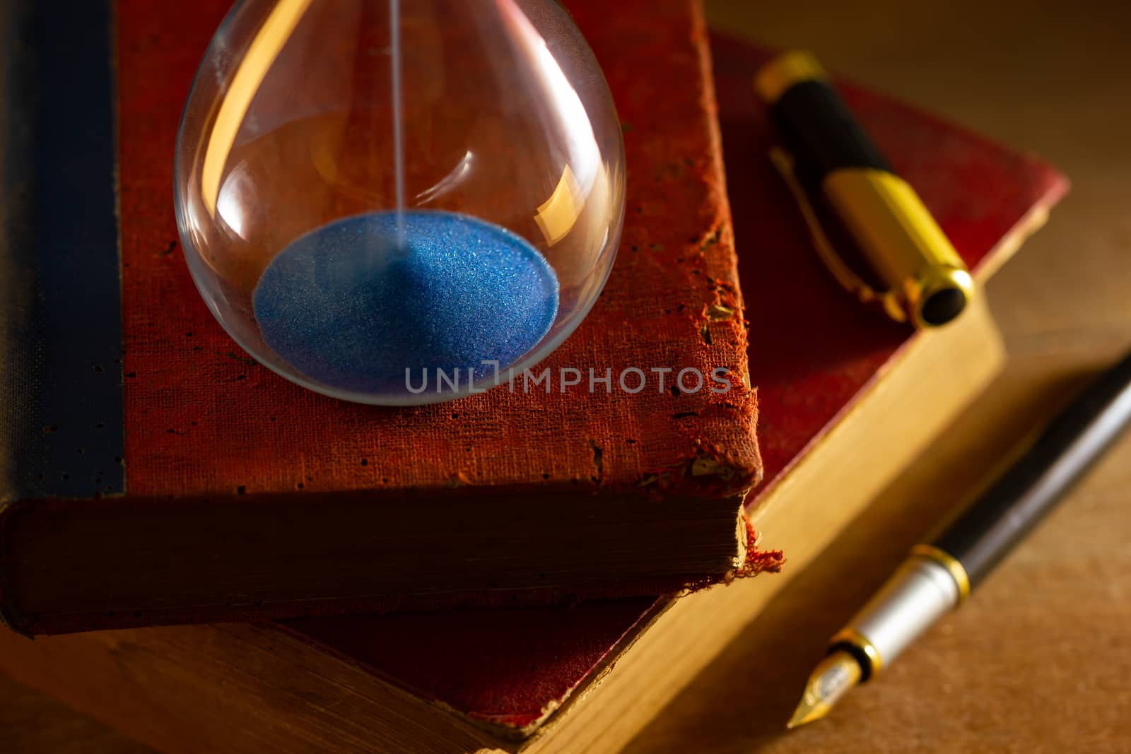 Hourglass on old book in morning light. Time of reading a book. by SaitanSainam