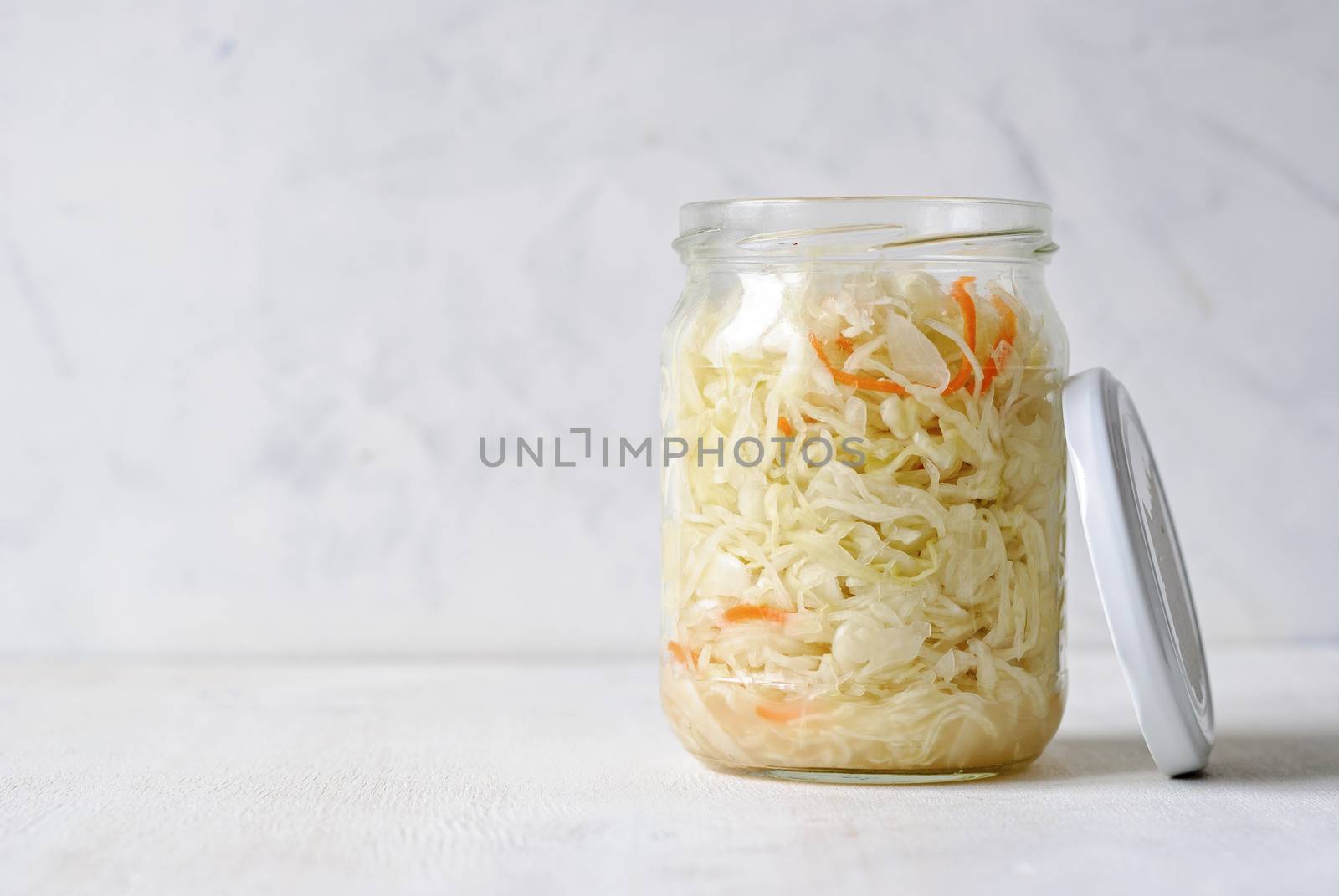 Transparent jar filled with juicy sauerkraut composed on white background