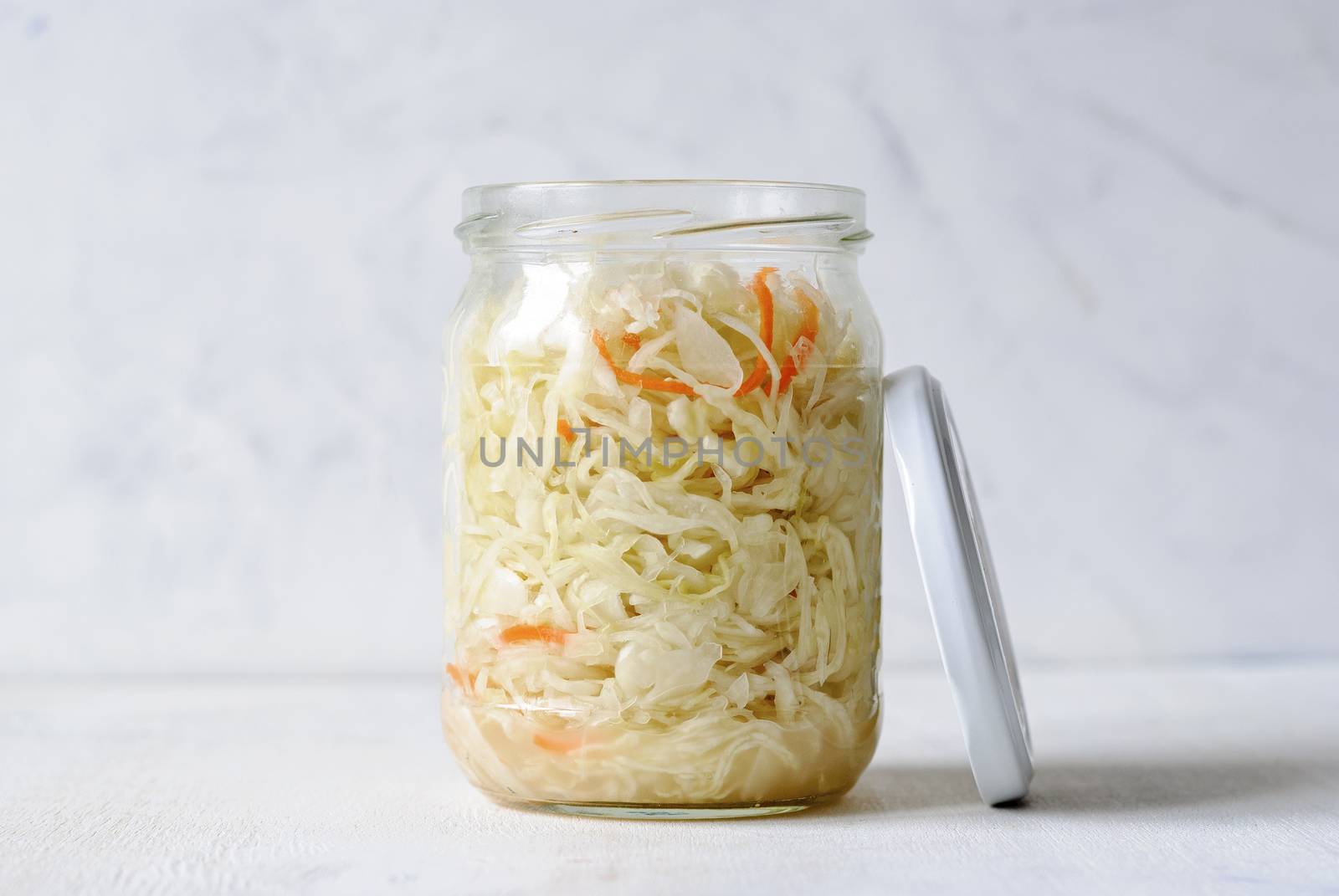 Transparent jar filled with juicy sauerkraut composed on white background