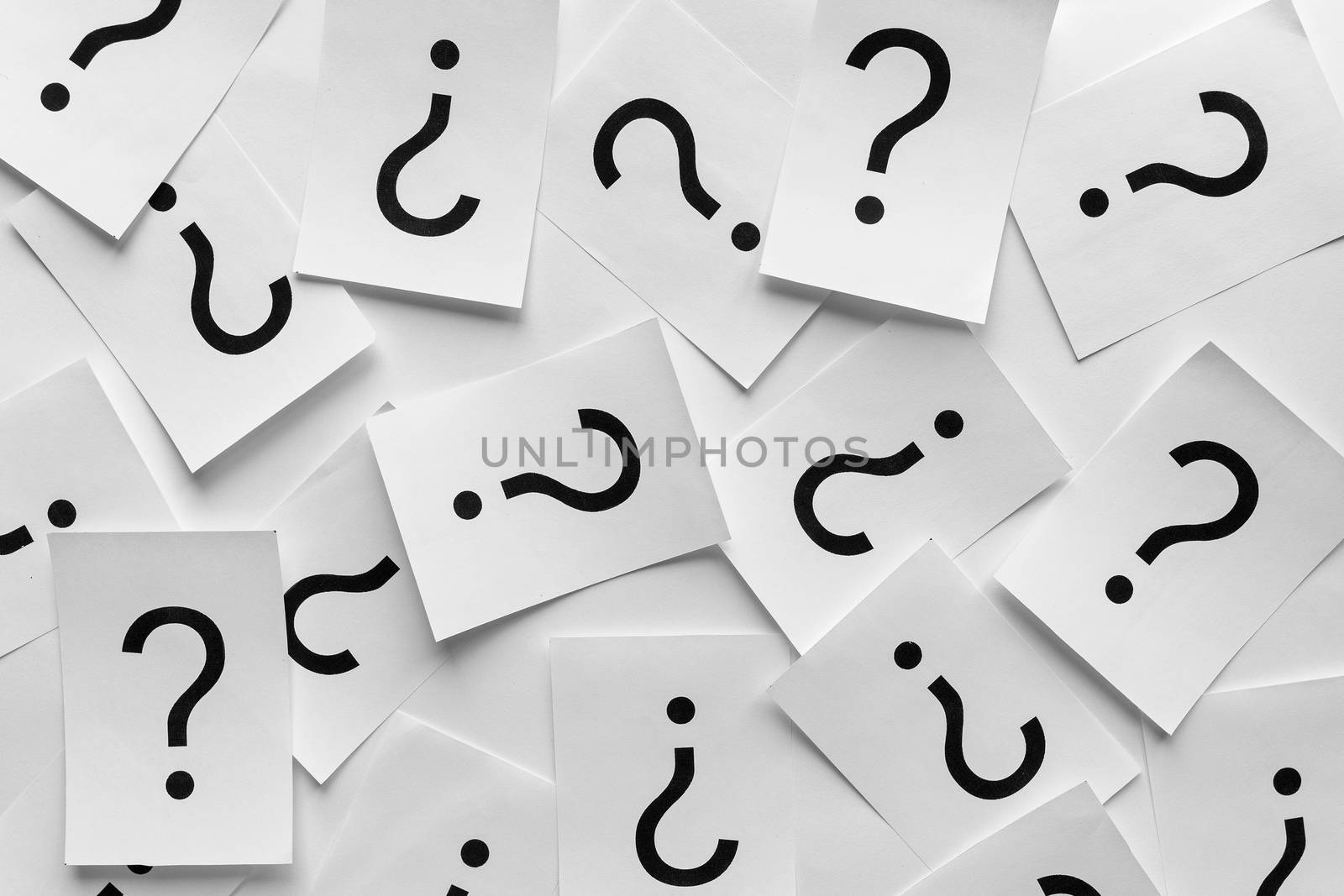 Background texture of printed question marks on white sheets of paper scattered randomly overlapping in a full frame view